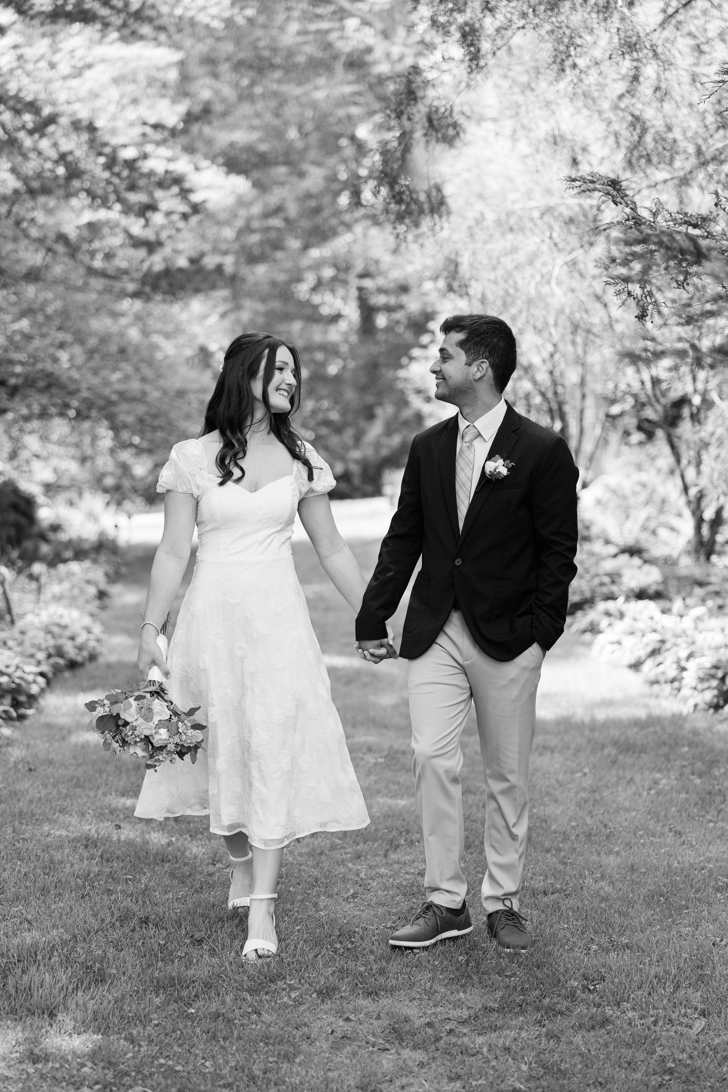 A black and white wedding photo of a couple walking together in a garden setting.