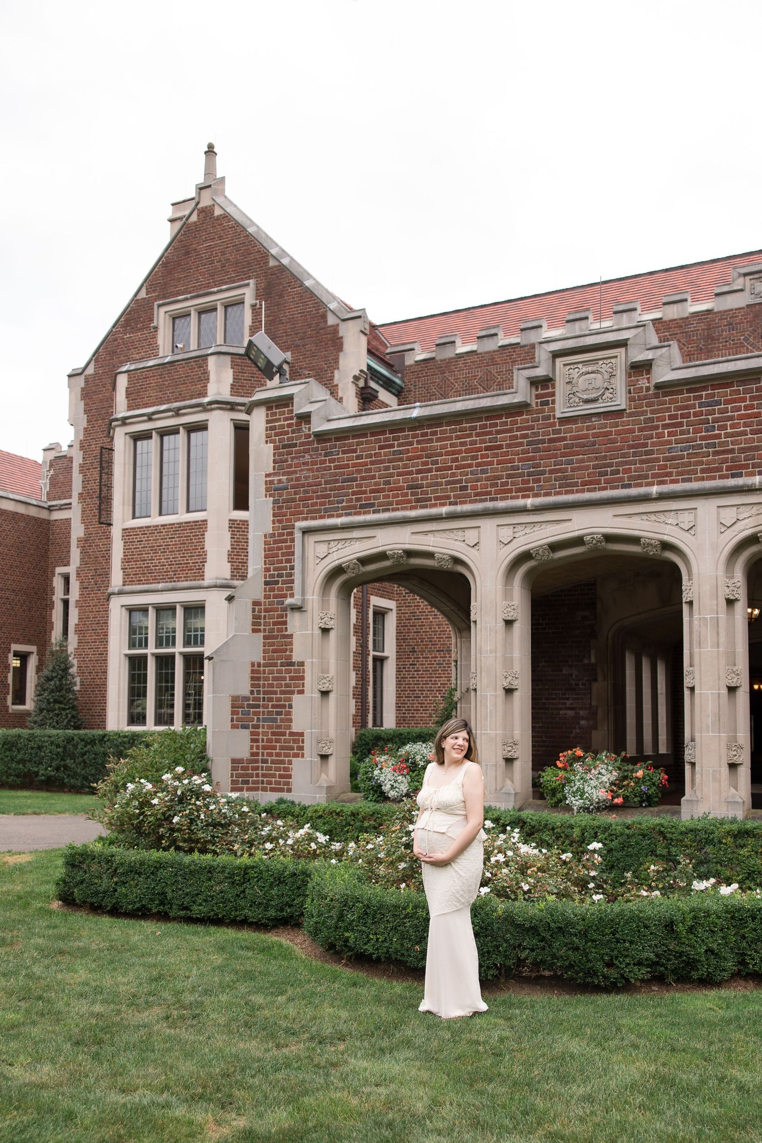 A gorgeous maternity photo taken in front of a historic Tudor-style brick building with manicured gardens.