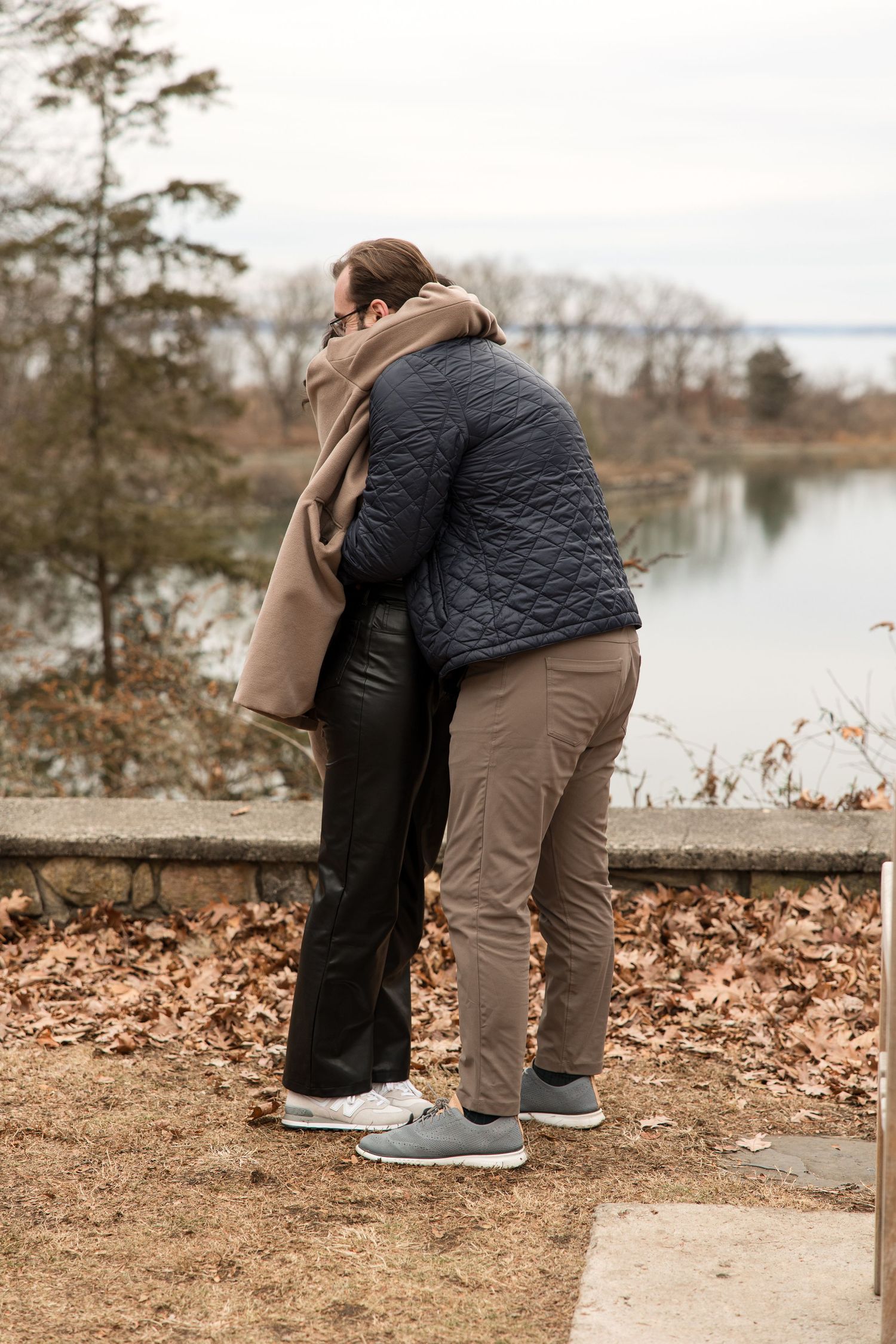 A tender embrace captured in profile against a lakeside backdrop.
