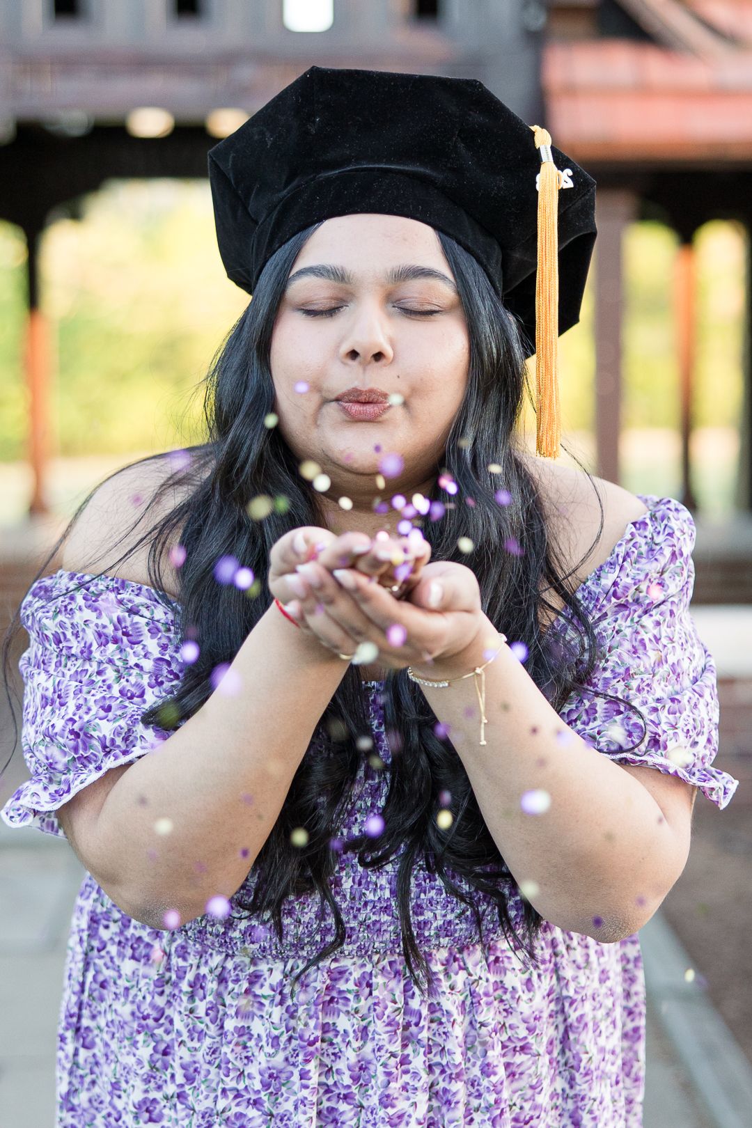 Graduate in cap and floral dress blows glitter in celebratory graduation photo.