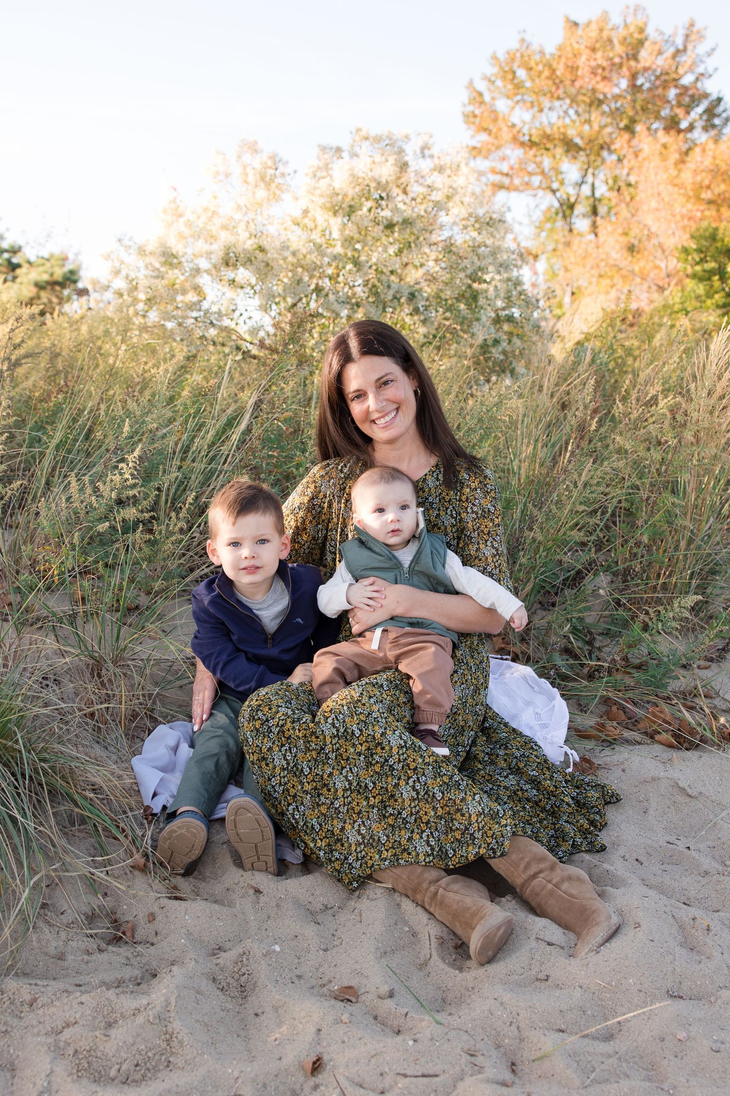 Family group seated on sandy beach dunes with coastal vegetation in background.