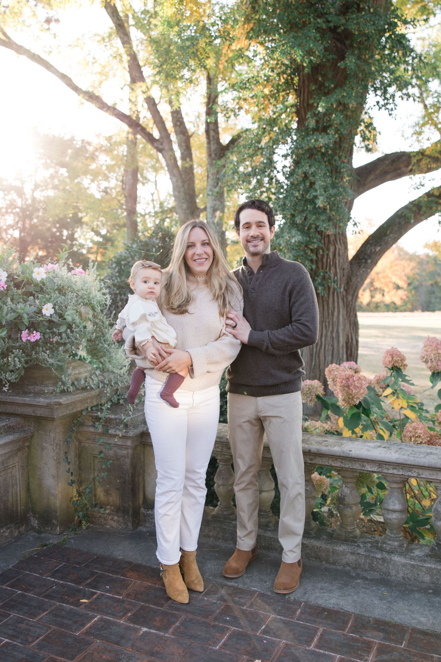 Family portrait outdoors with autumn trees and garden setting.