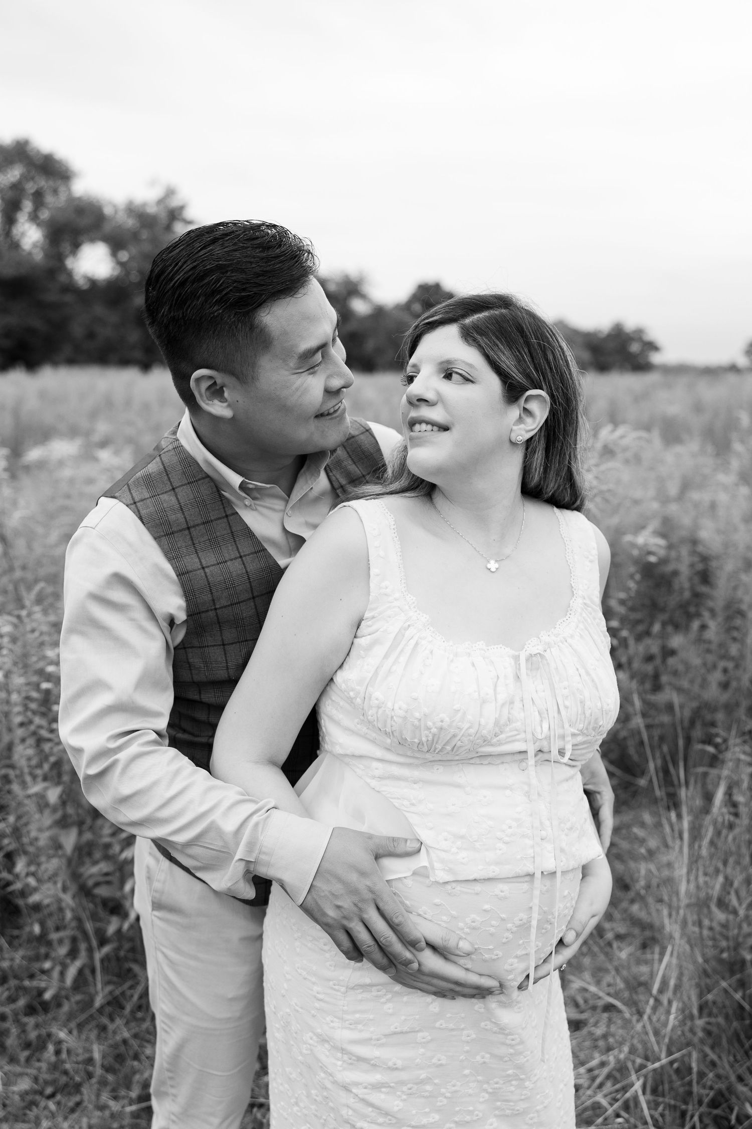 Joyful maternity portrait of couple laughing together in natural outdoor setting.