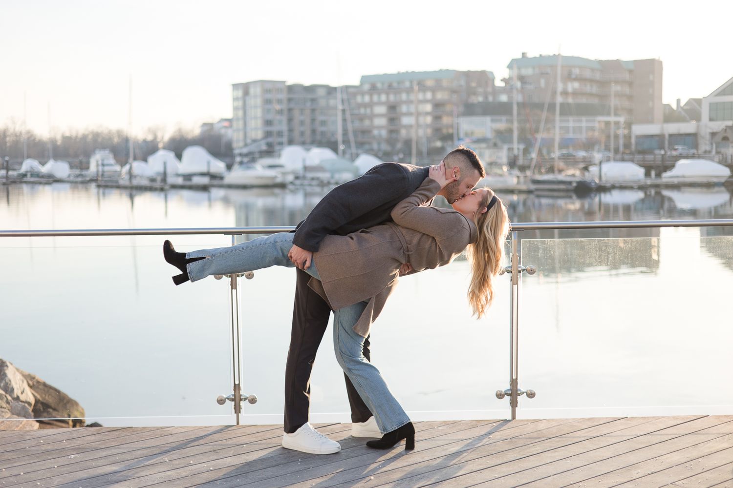 A romantic dip pose on a waterfront dock with boats in the background.