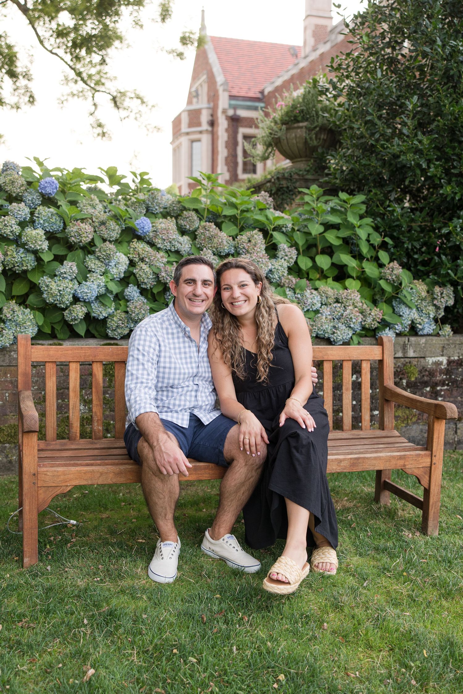 A couple sits together on a wooden bench surrounded by blooming hydrangeas and garden scenery.