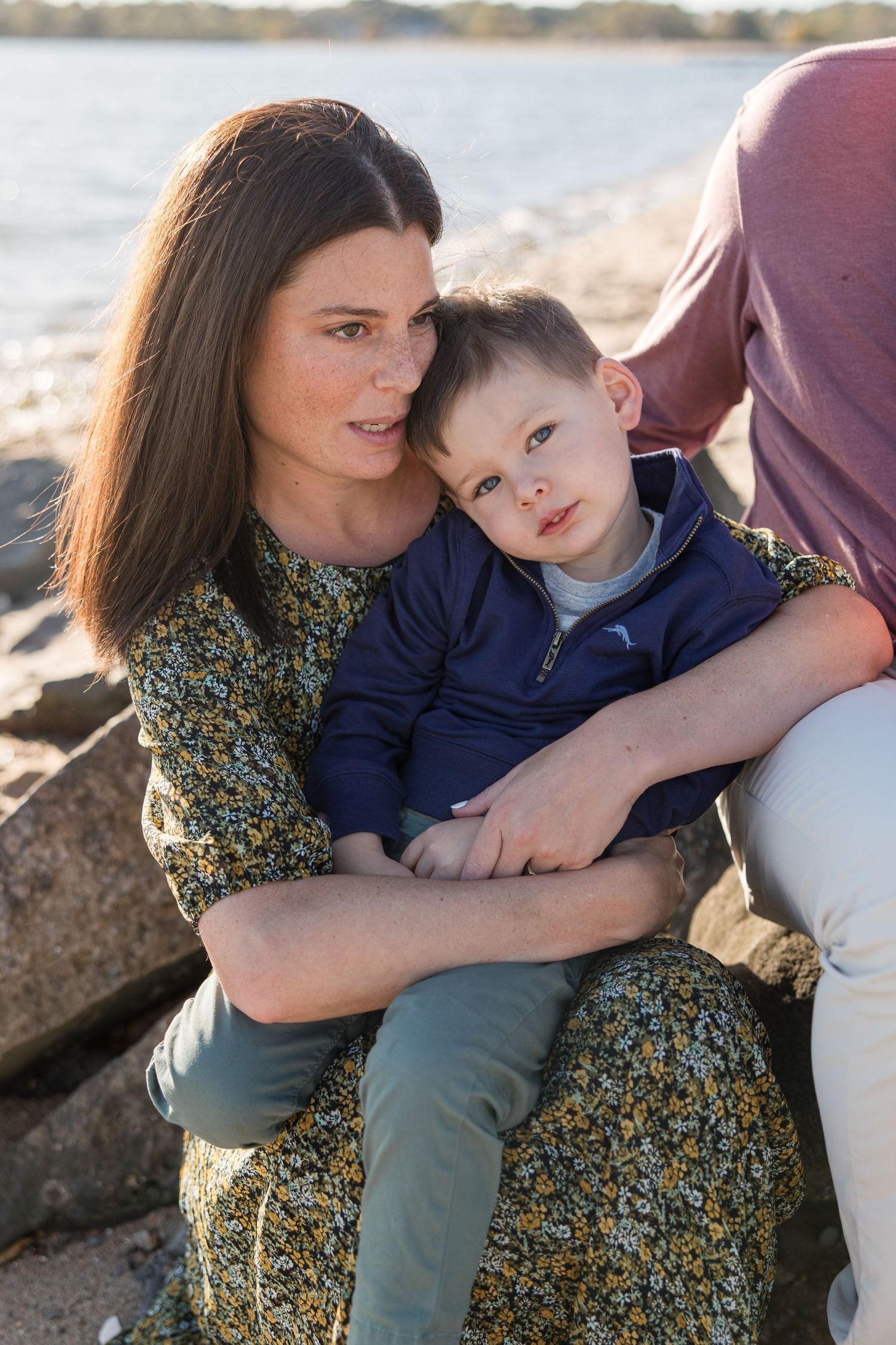 Mother and child sharing tender moment on rocky beach at sunset.