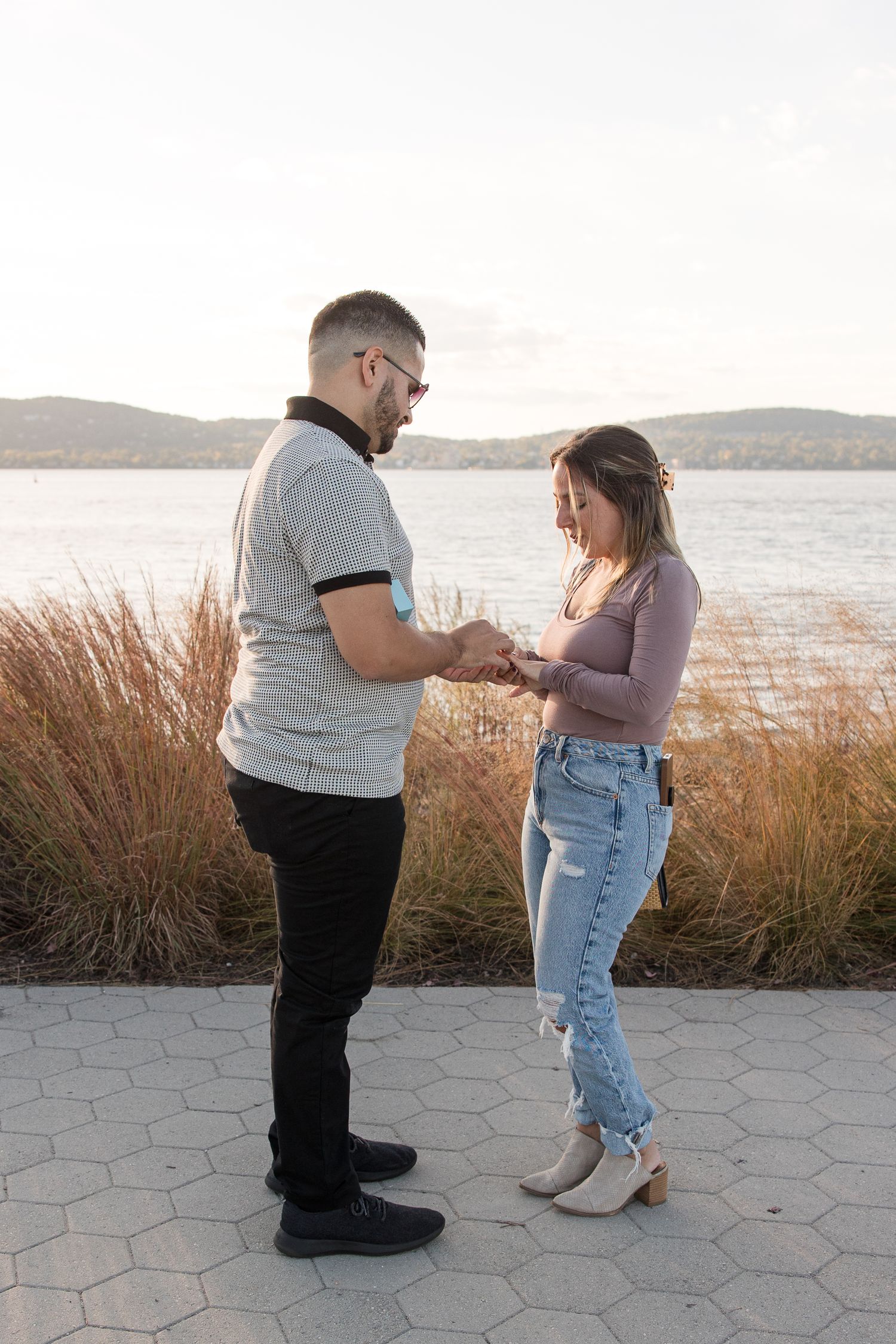 Couple examining engagement ring by lighthouse with water view.