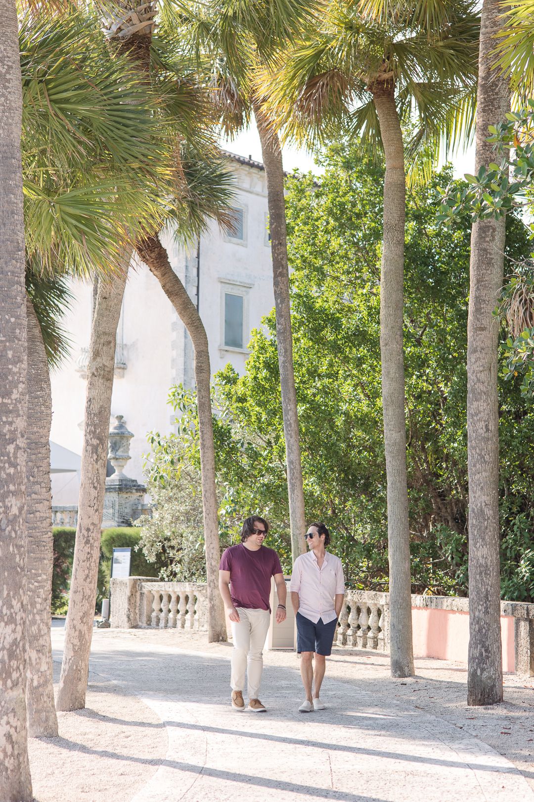 Two people strolling down a palm-lined pathway near a white building.
