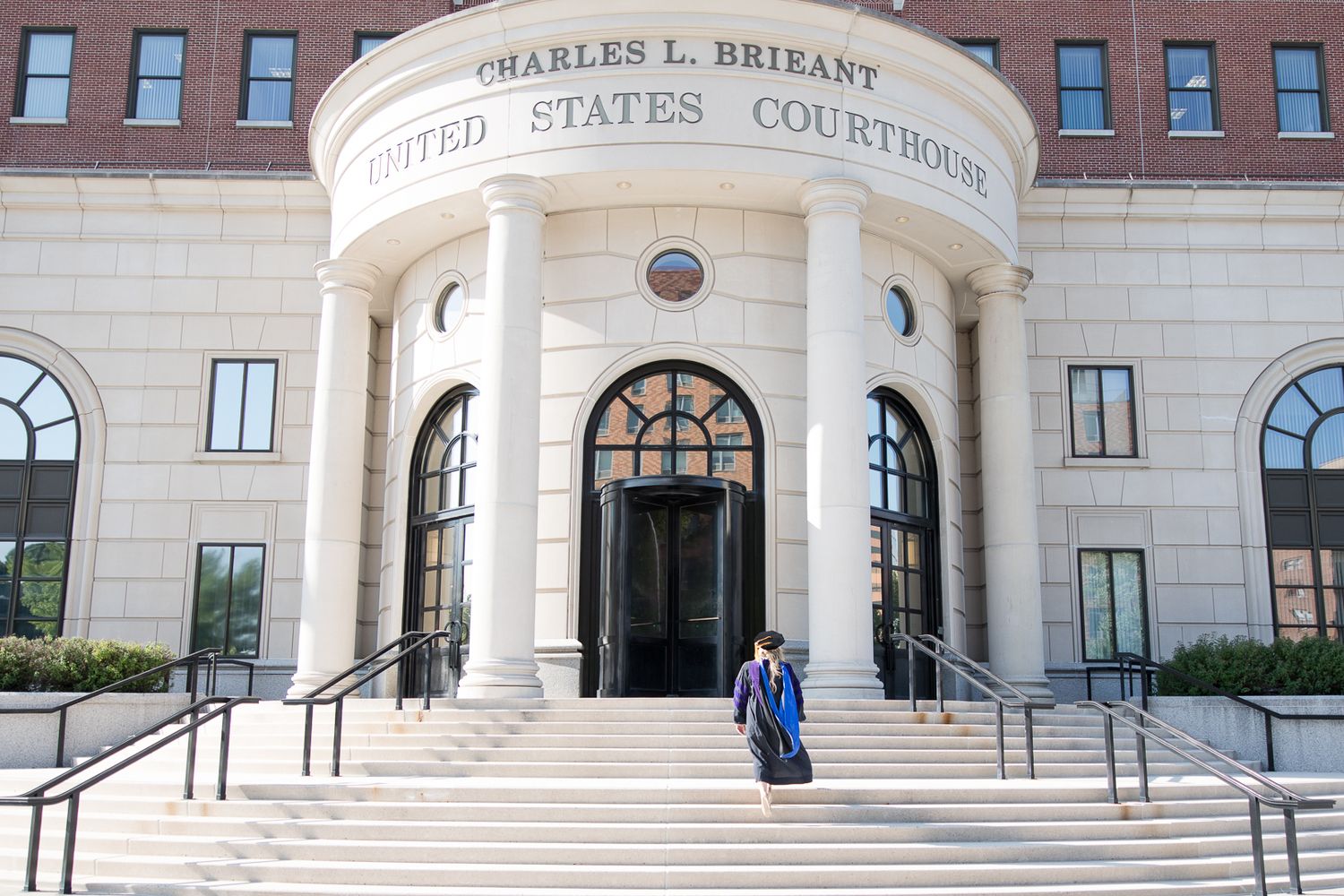 Graduate in blue and purple regalia posed on the steps of federal courthouse.