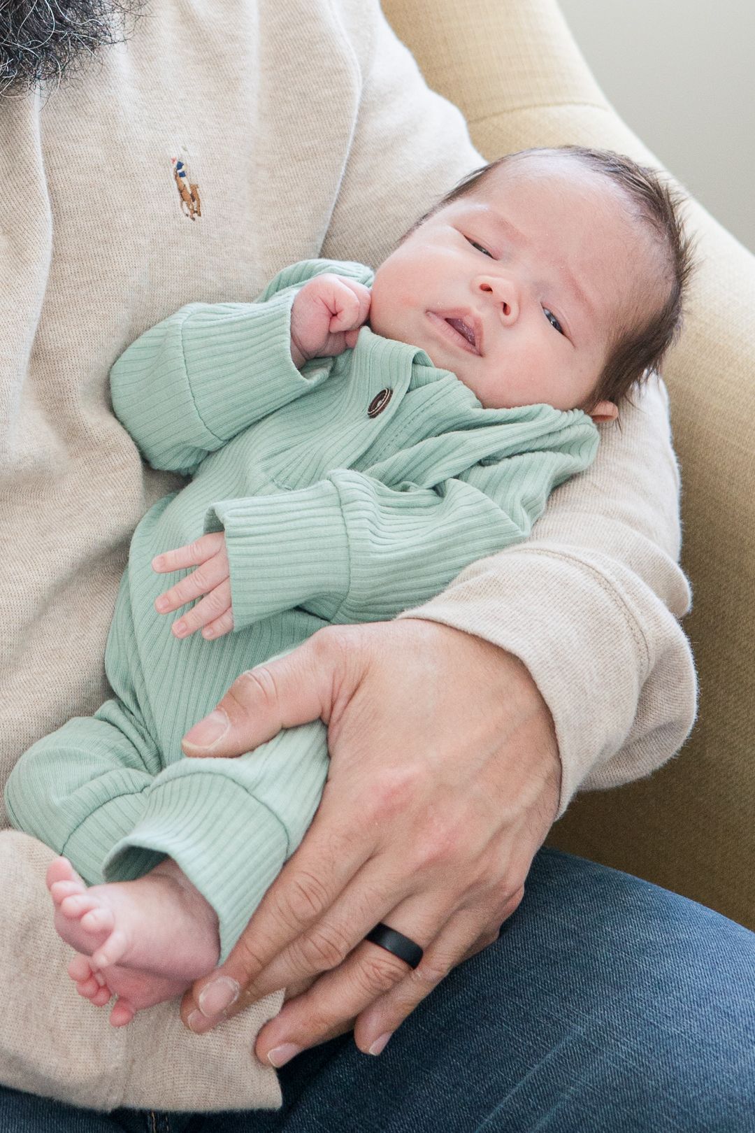 Sleeping baby in mint green ribbed outfit rests peacefully in adult's arms.