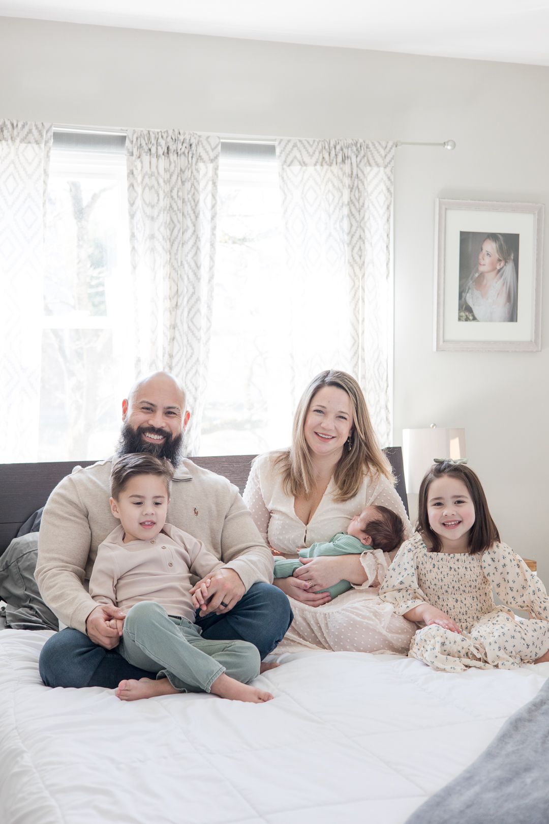 Family portrait on bed with children and geometric curtains in bright room.