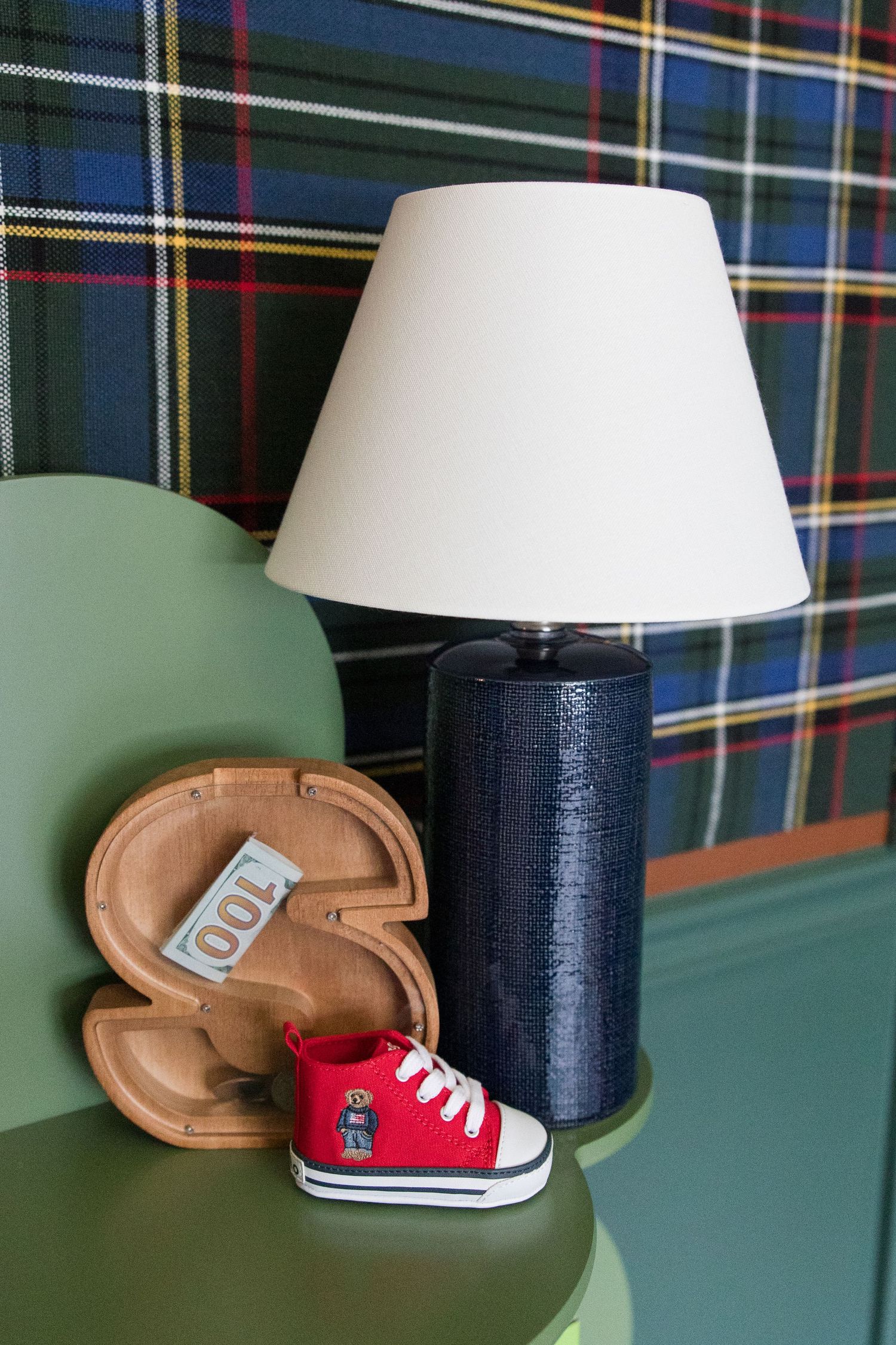 Navy blue table lamp with white shade next to decorative wooden letter and red baby shoe.