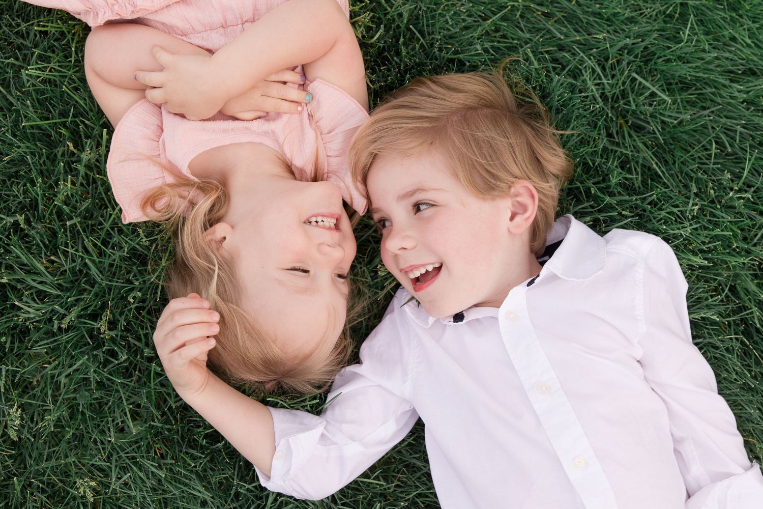 Two people in white clothing lying on green grass share sweet, close moments together in a candid photo series.