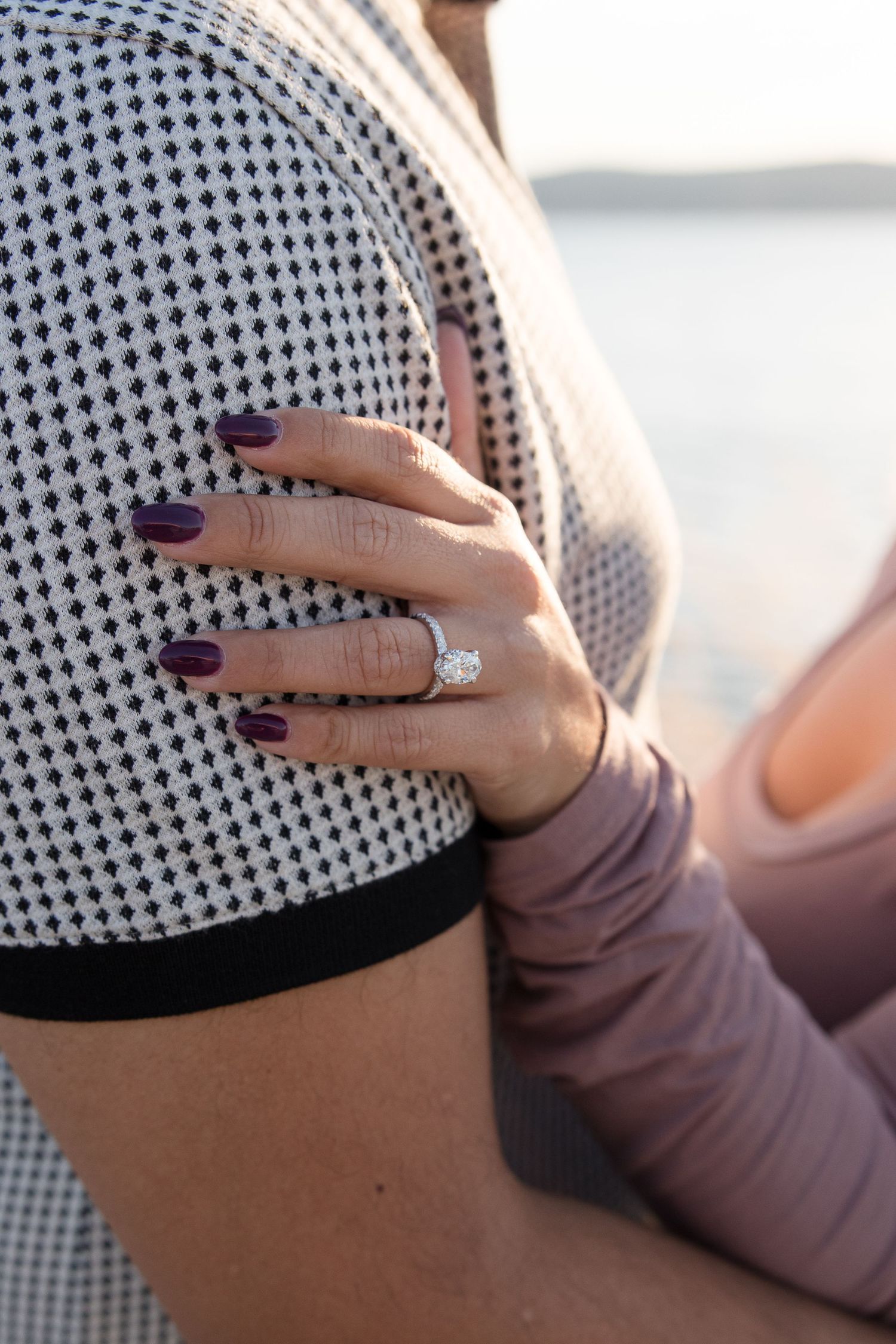Close-up of purple manicured nails and engagement ring against checkered fabric.