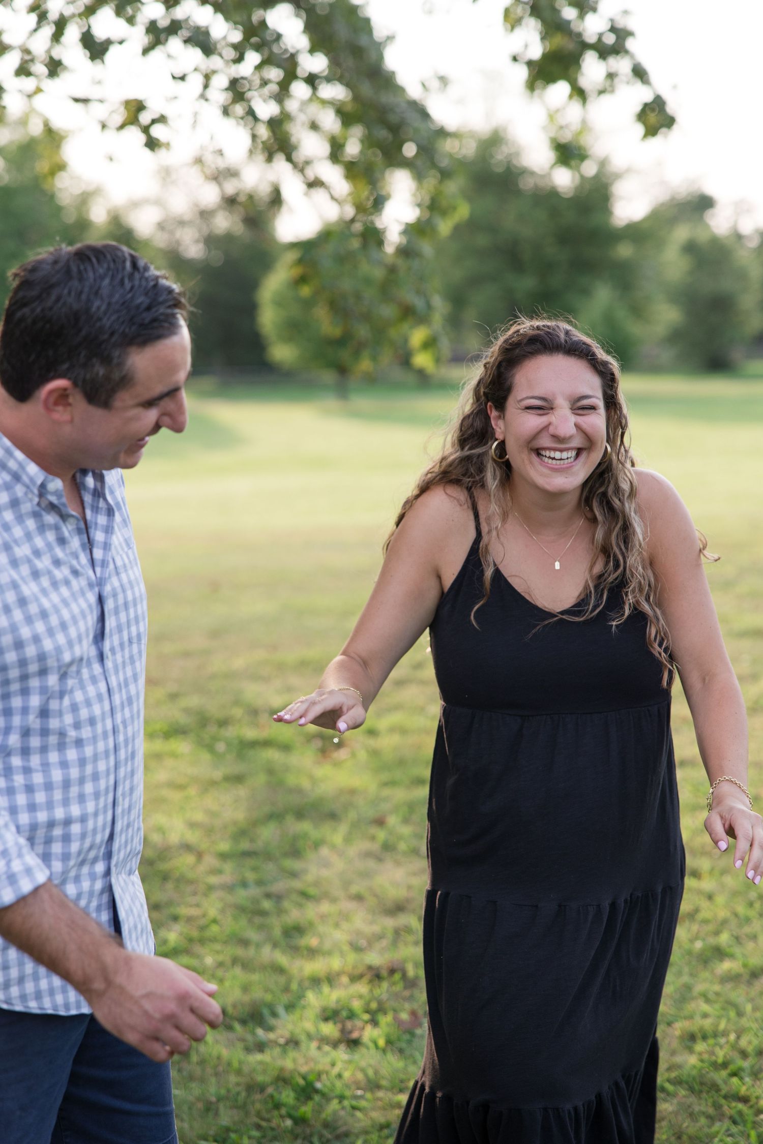 A couple shares a candid laughing moment together in a sunny outdoor garden setting.