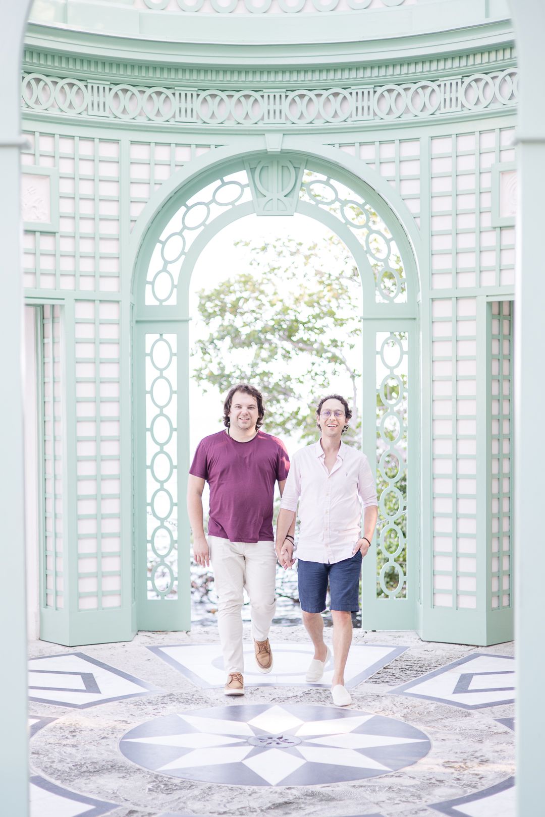 Two people stand in an ornate mint green and white gazebo with intricate architectural details.