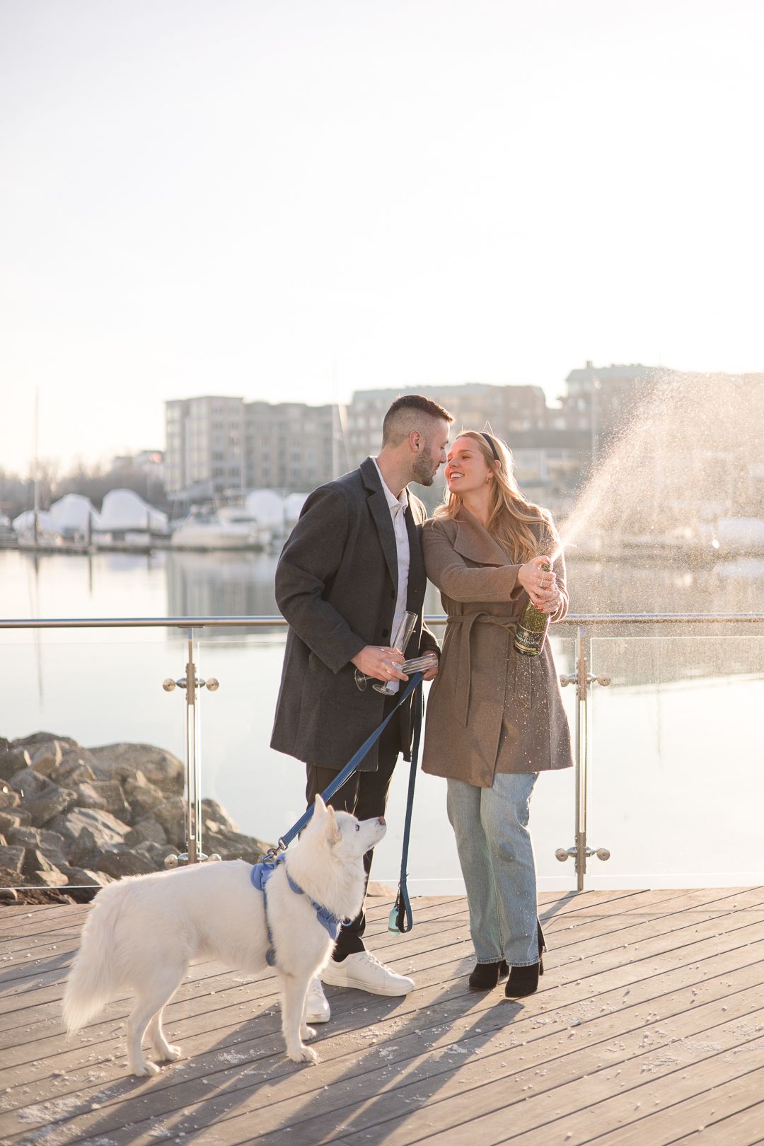 Romantic moment shared between couple with white dog on marina boardwalk.
