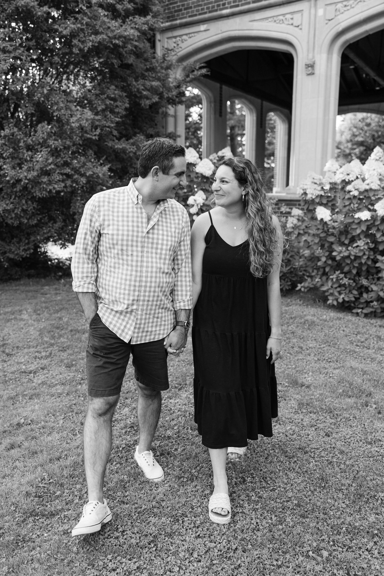 A black and white photo of a couple walking together near an arched building entrance.