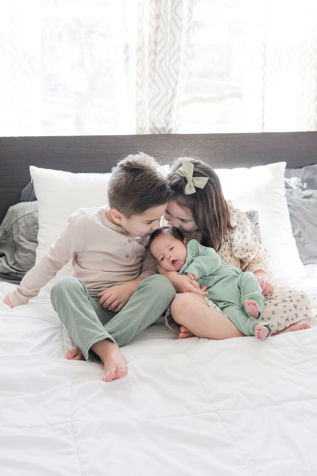 Family cuddles together on white bed wearing coordinated neutral and mint green outfits.