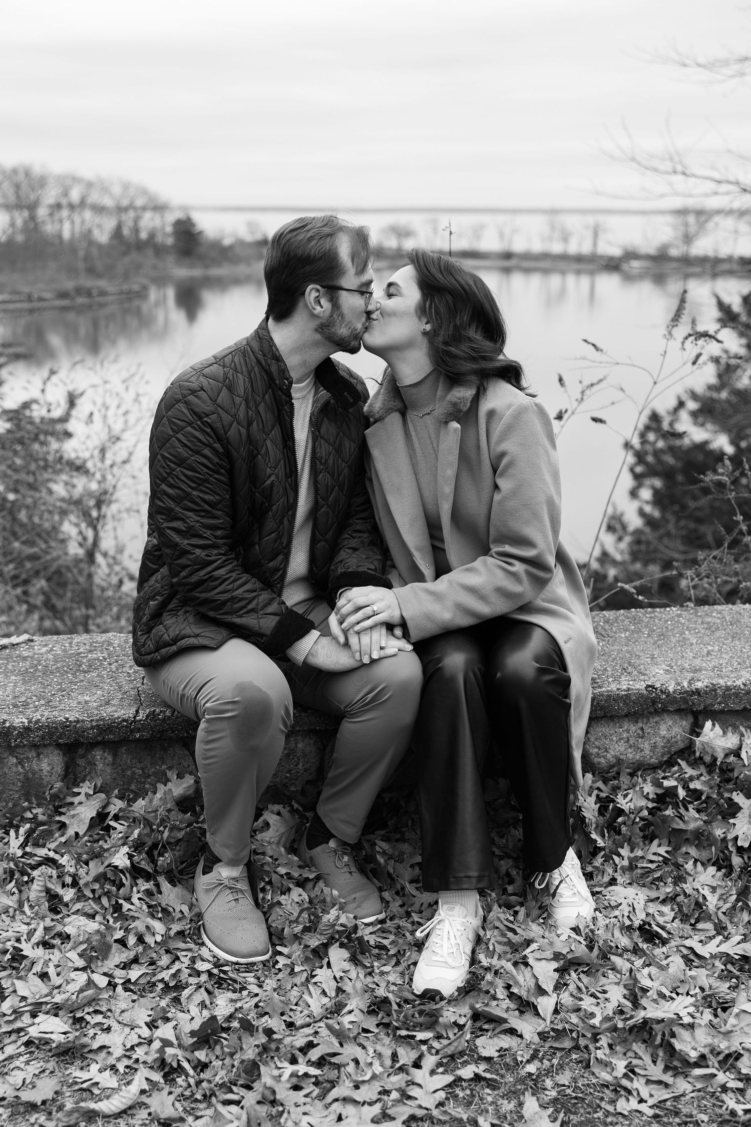 A couple sitting together and sharing a tender kiss on a fall day by a scenic lake.