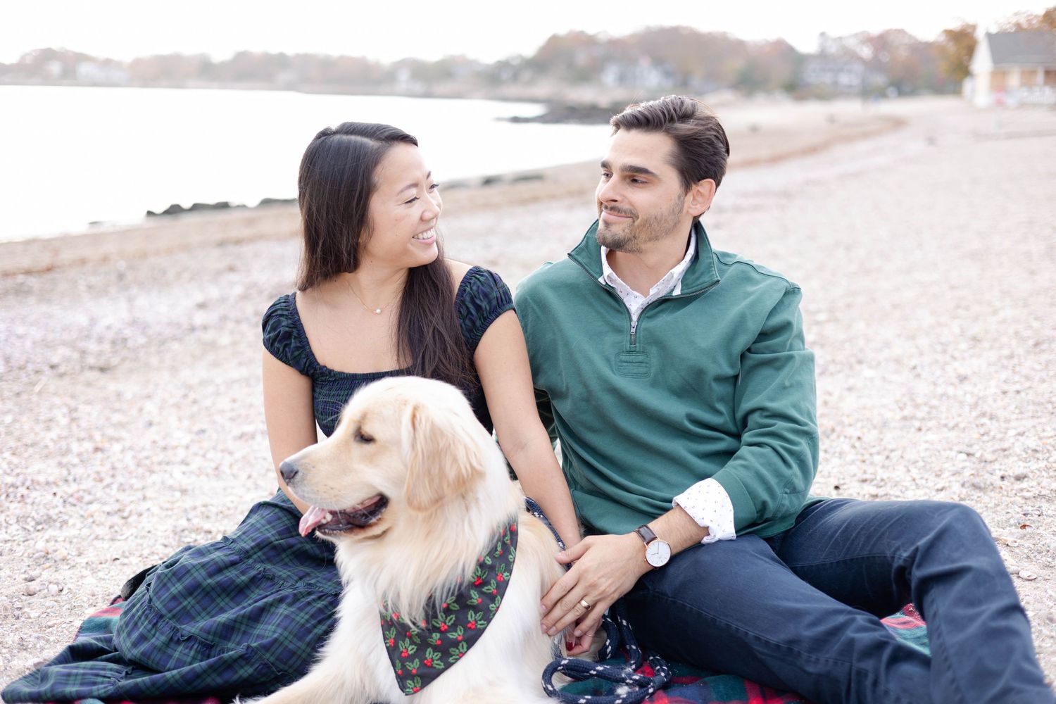 A couple and their golden retriever share a tender moment on a picturesque beach blanket at sunset.