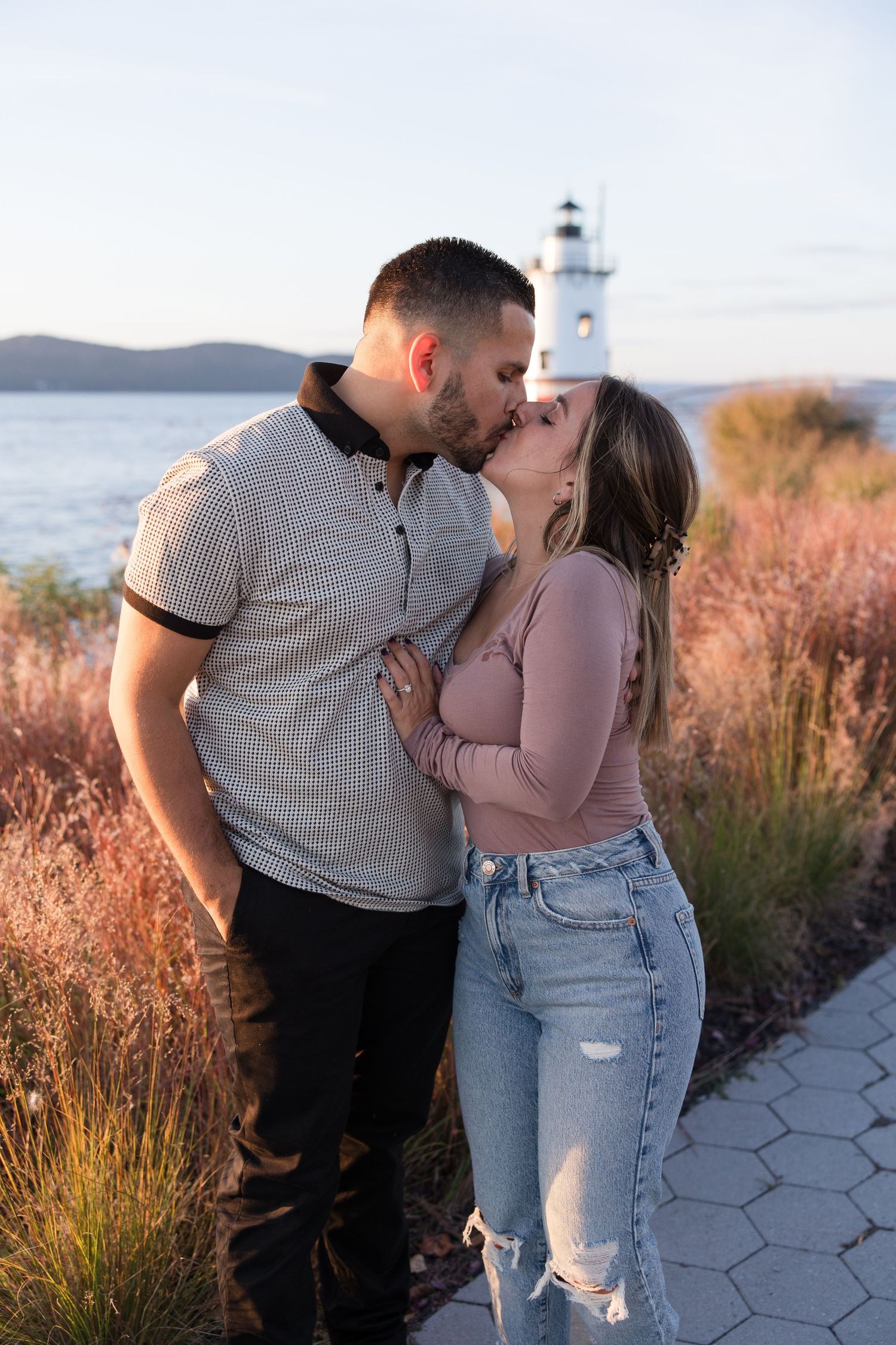Romantic moment shared near lighthouse with tall grasses in foreground.