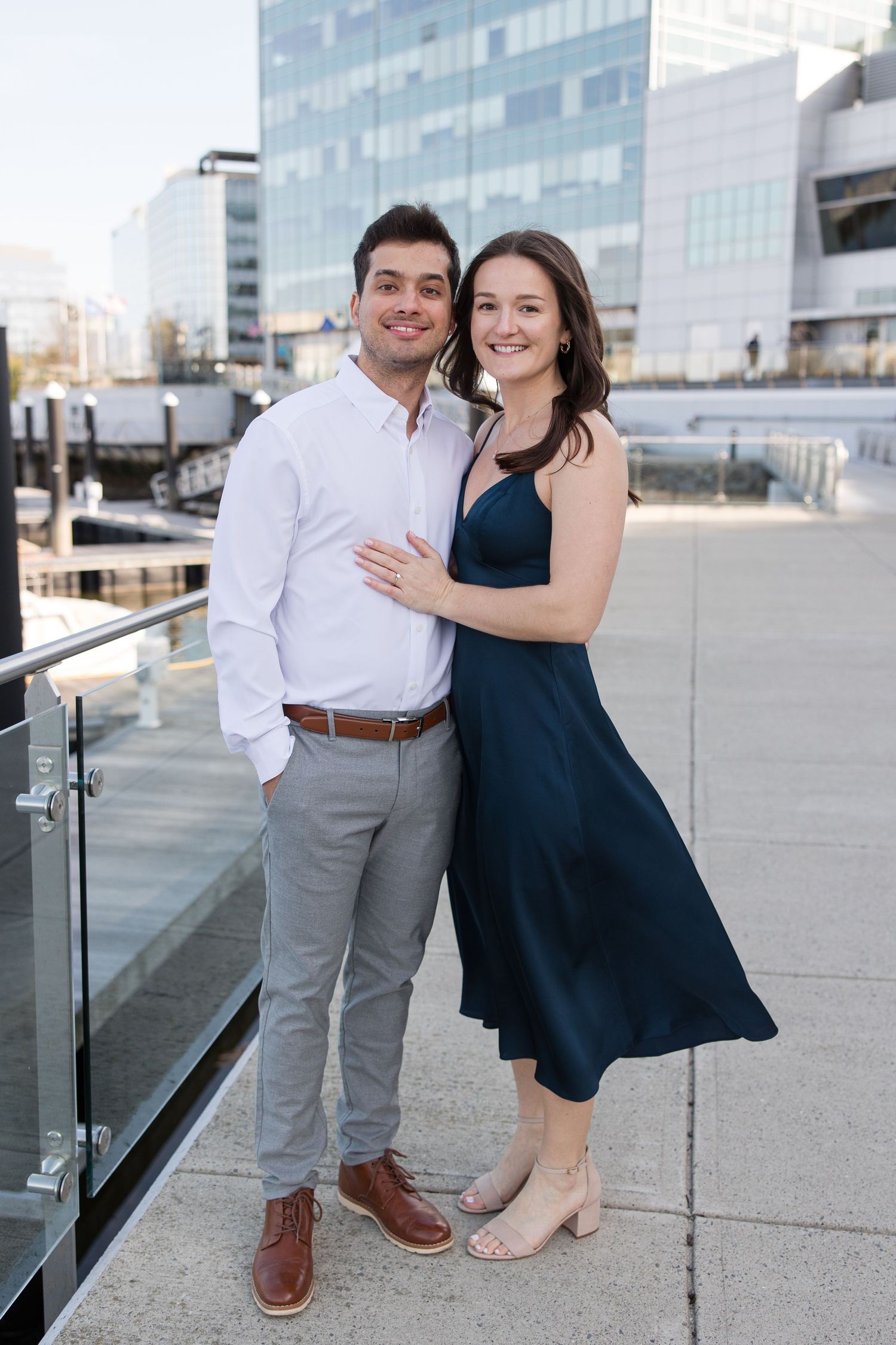 Happy couple in navy dress and white shirt pose together on urban waterfront.