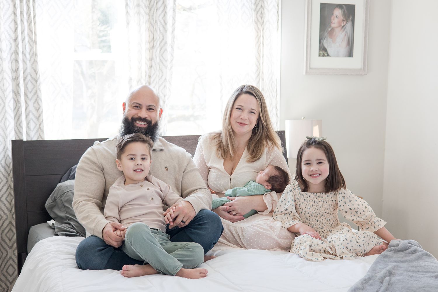 Intimate family portrait on a cozy bed with neutral tones and natural window light.