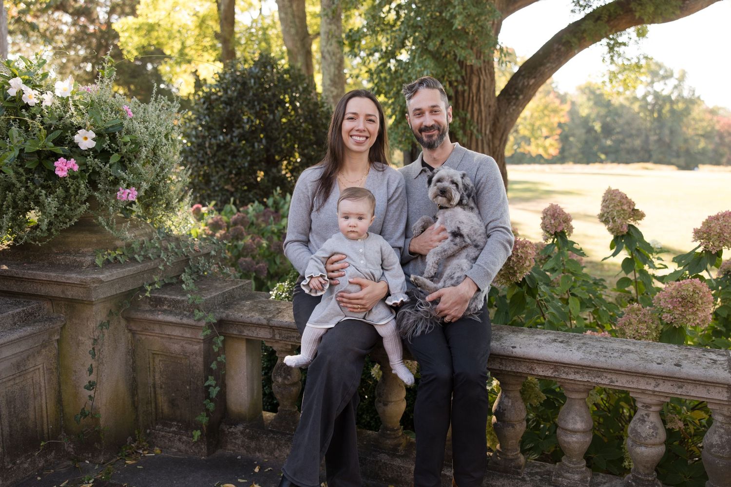 Family portrait captured on stone bench in garden setting with pet dog.