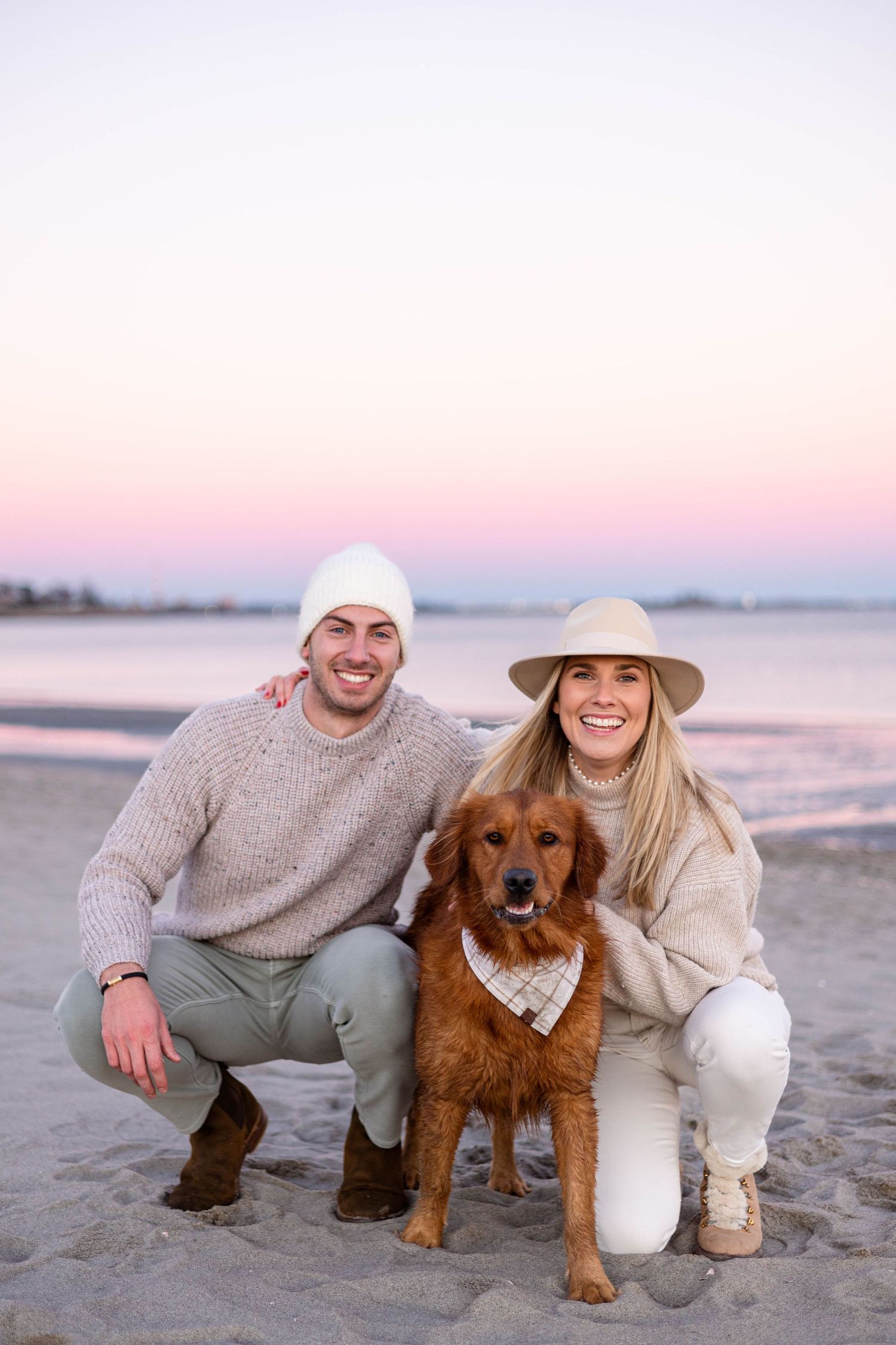 Couple with their golden retriever dog posing on beach at sunset.