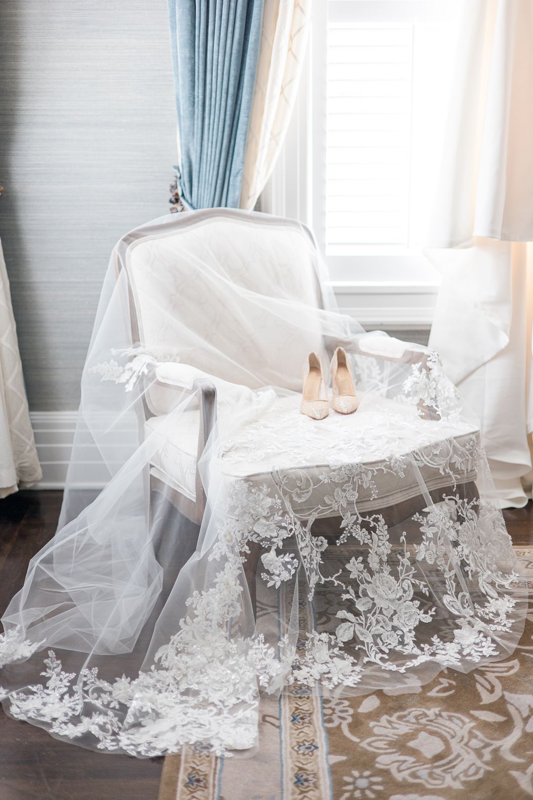 Wedding accessories including a lace veil and beige heels arranged on an ornate chair.