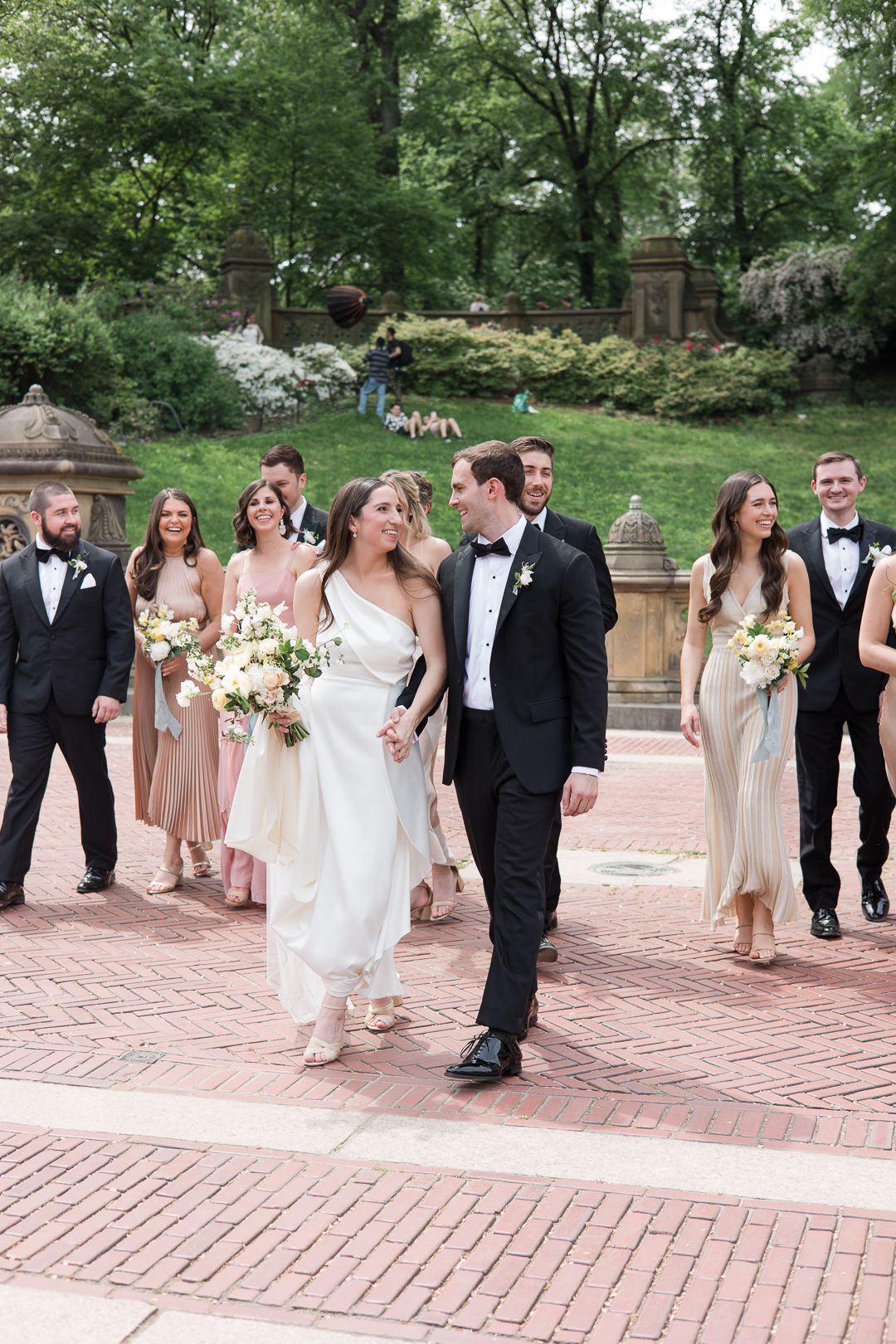 Wedding party walking together on brick pathway surrounded by spring blooms.