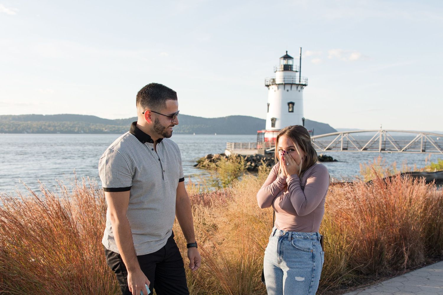 Couple enjoying a lighthearted conversation by a scenic lighthouse and waterfront.