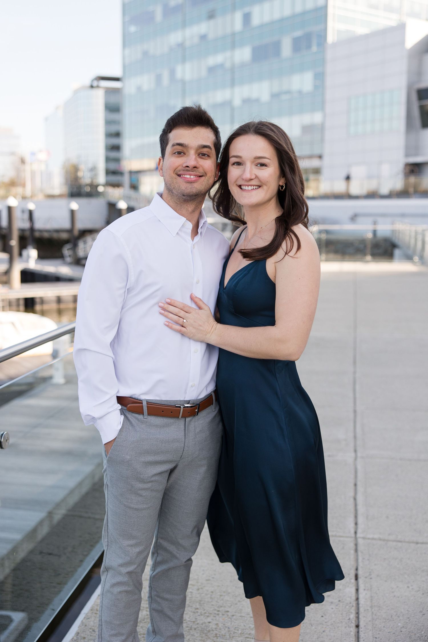 Couple in formal attire posing together on an urban rooftop deck with modern buildings in the background.