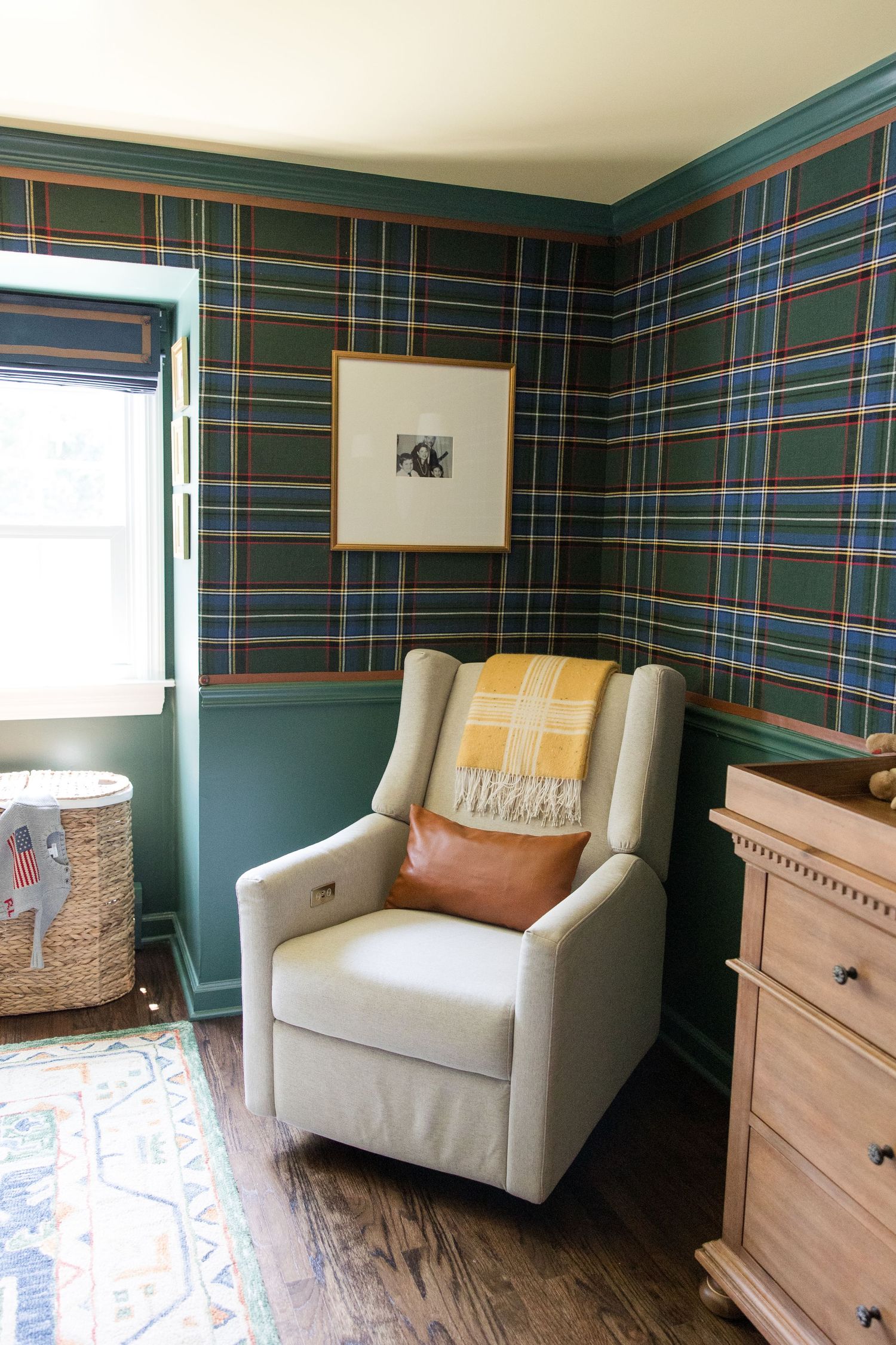 A cozy nursery corner featuring a beige recliner, plaid wallpaper, and wooden furniture.