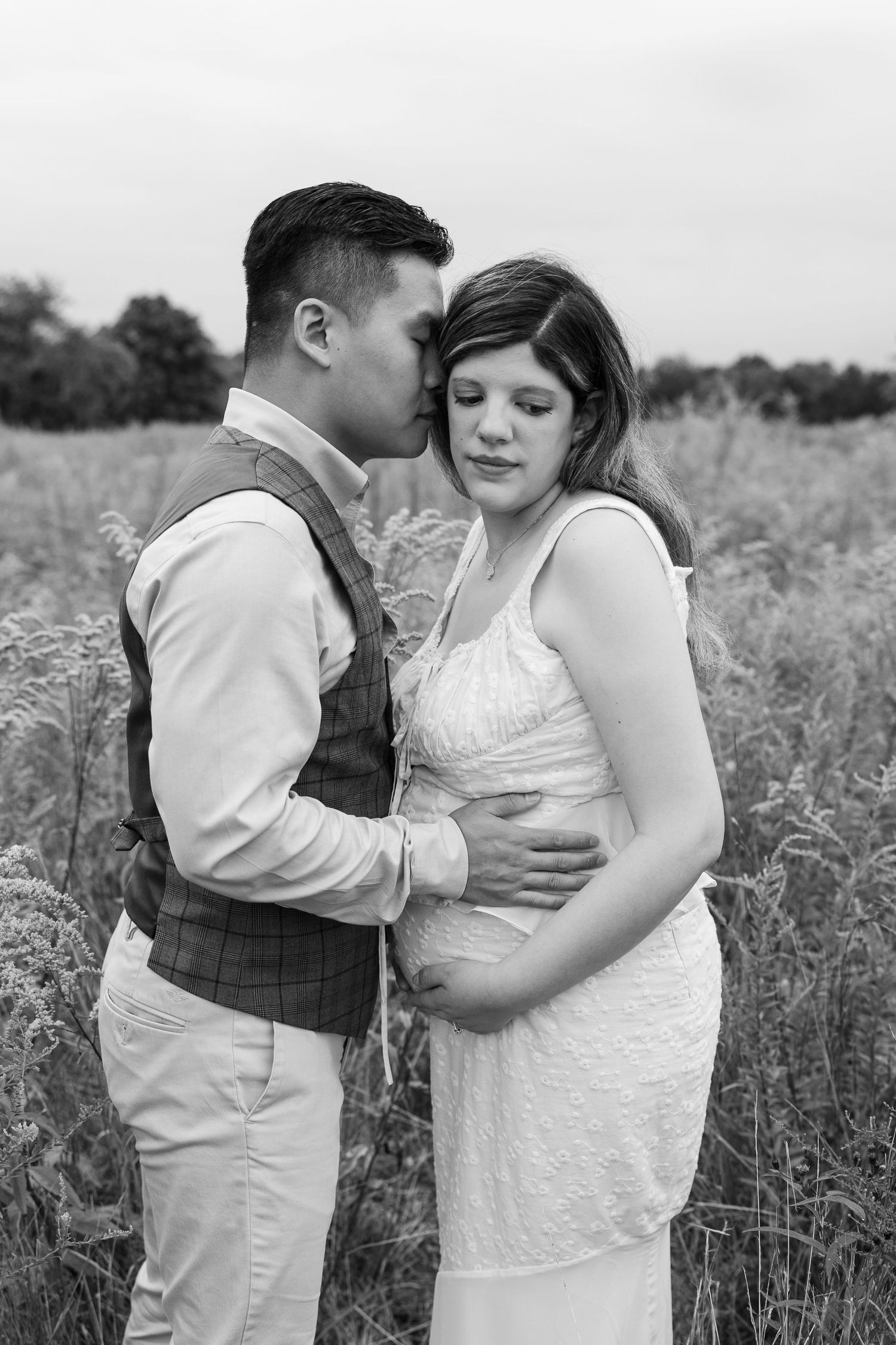Intimate black and white maternity photo of couple embracing in a wild meadow setting.