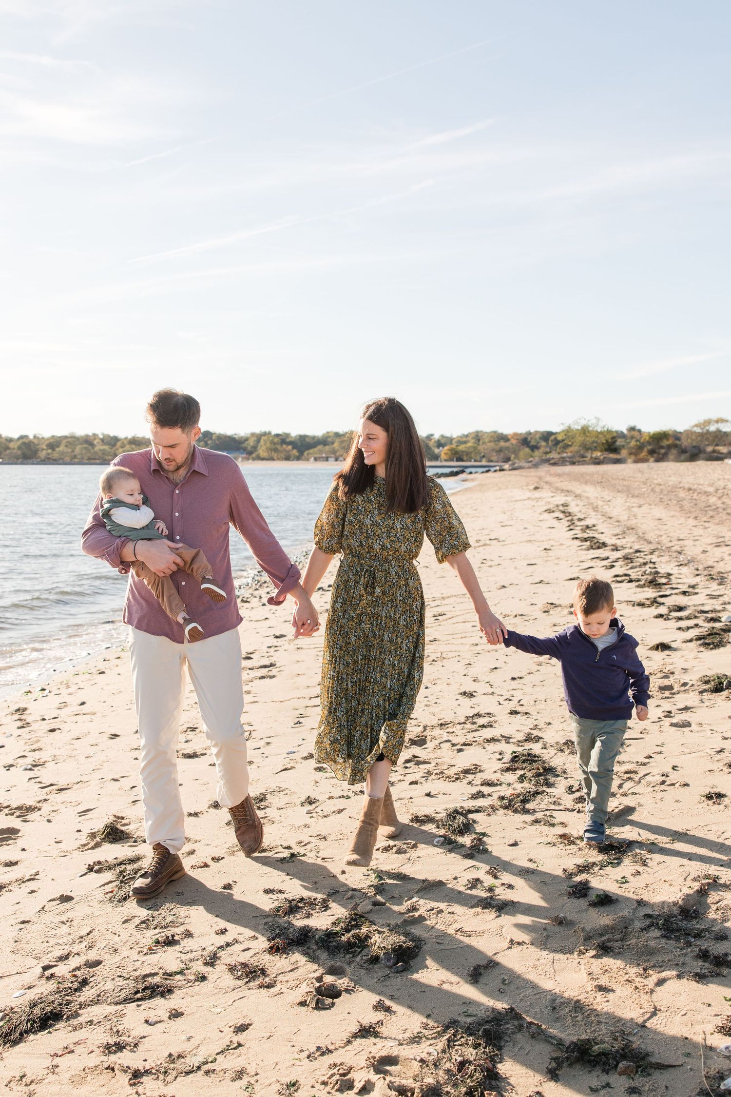 Family walking hand in hand along shoreline with water and beaches in background.