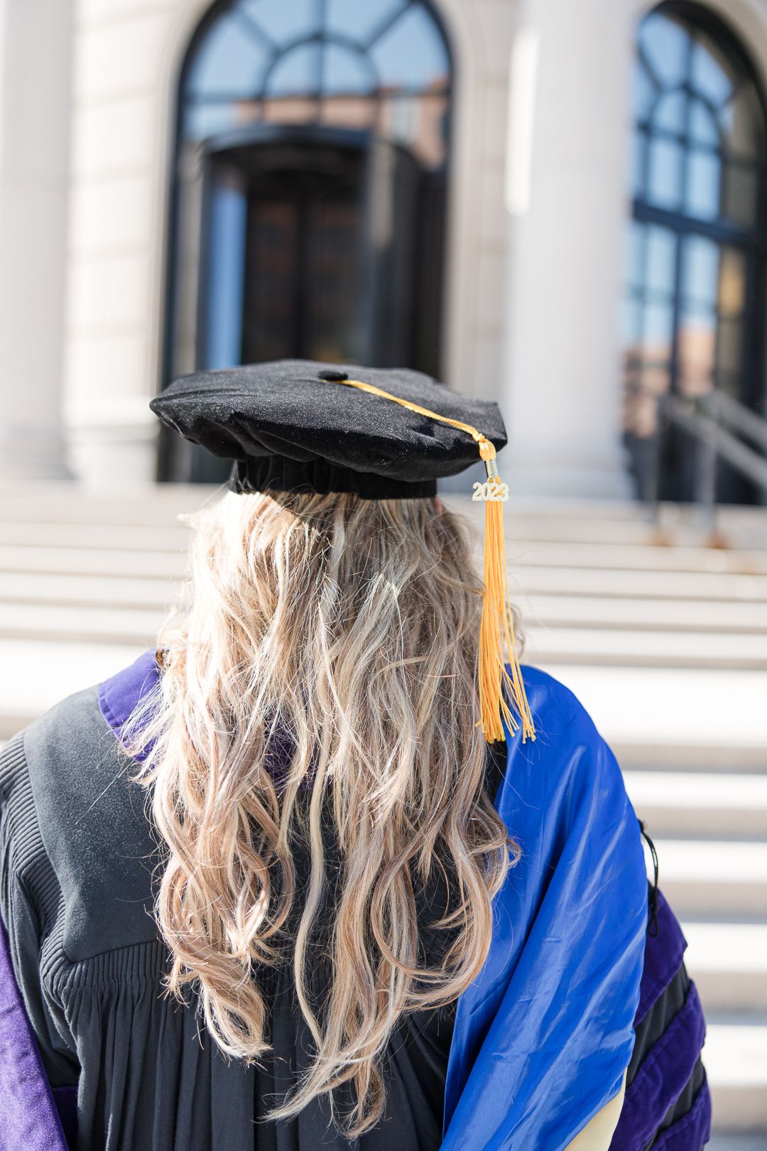 Back view of graduation cap with gold tassel and blonde hair at courthouse.