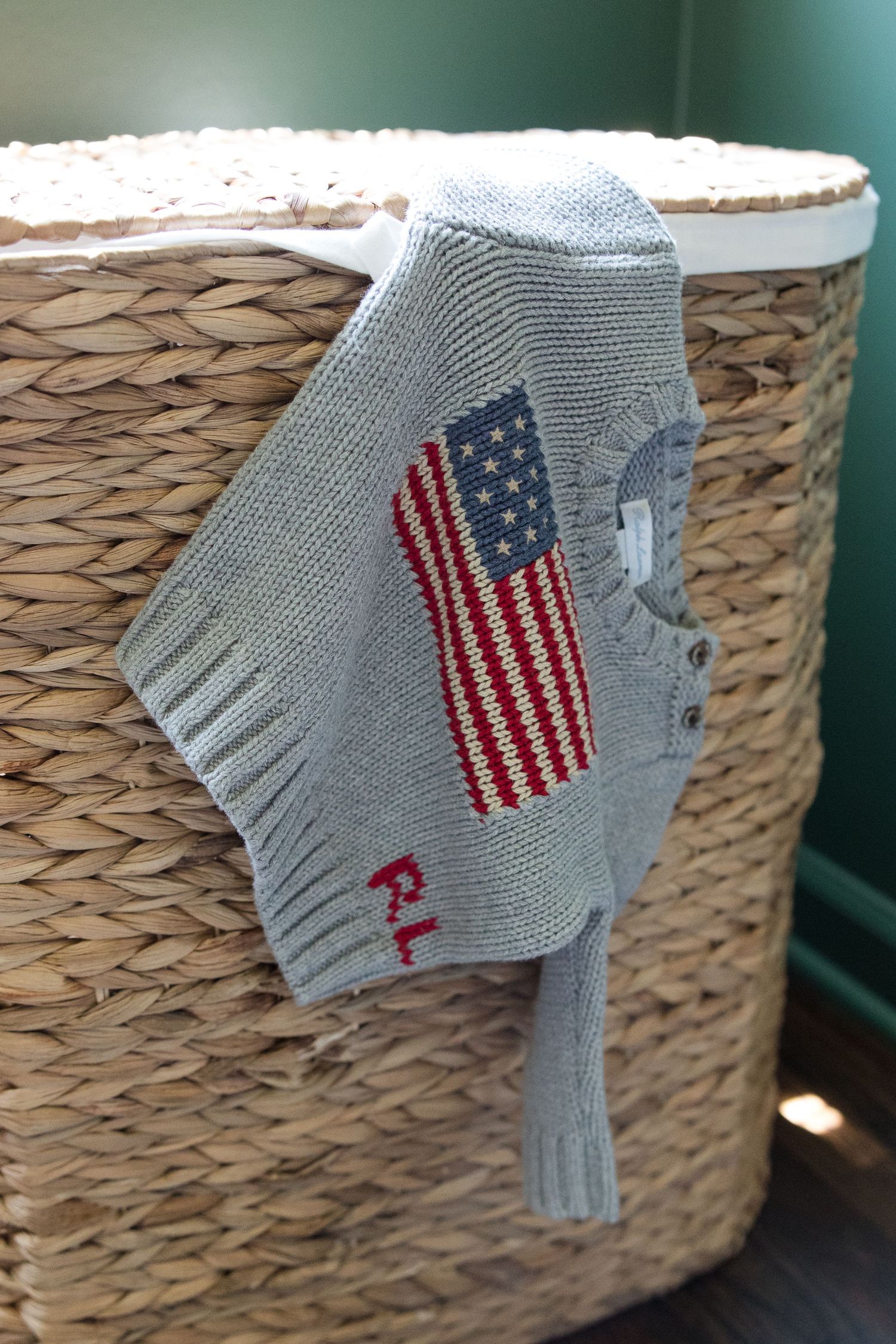 A gray baby sock with an American flag design hangs on the edge of a woven basket.
