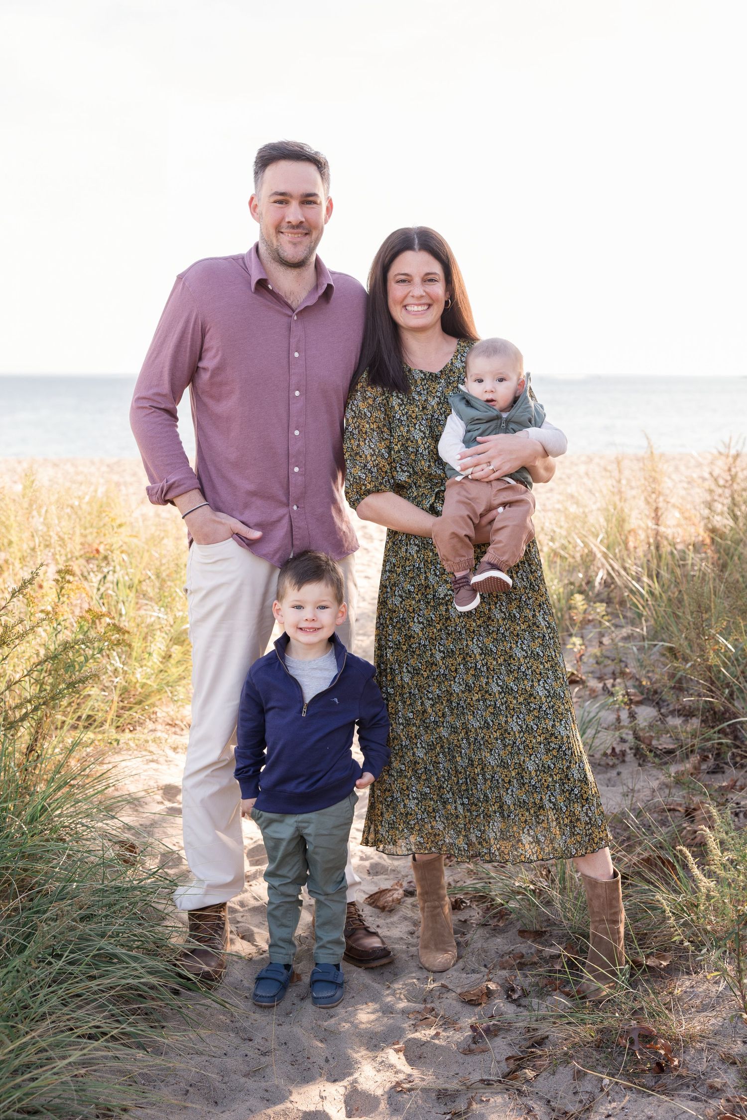 Family portrait on a beach with golden grasses and soft lighting at sunset.