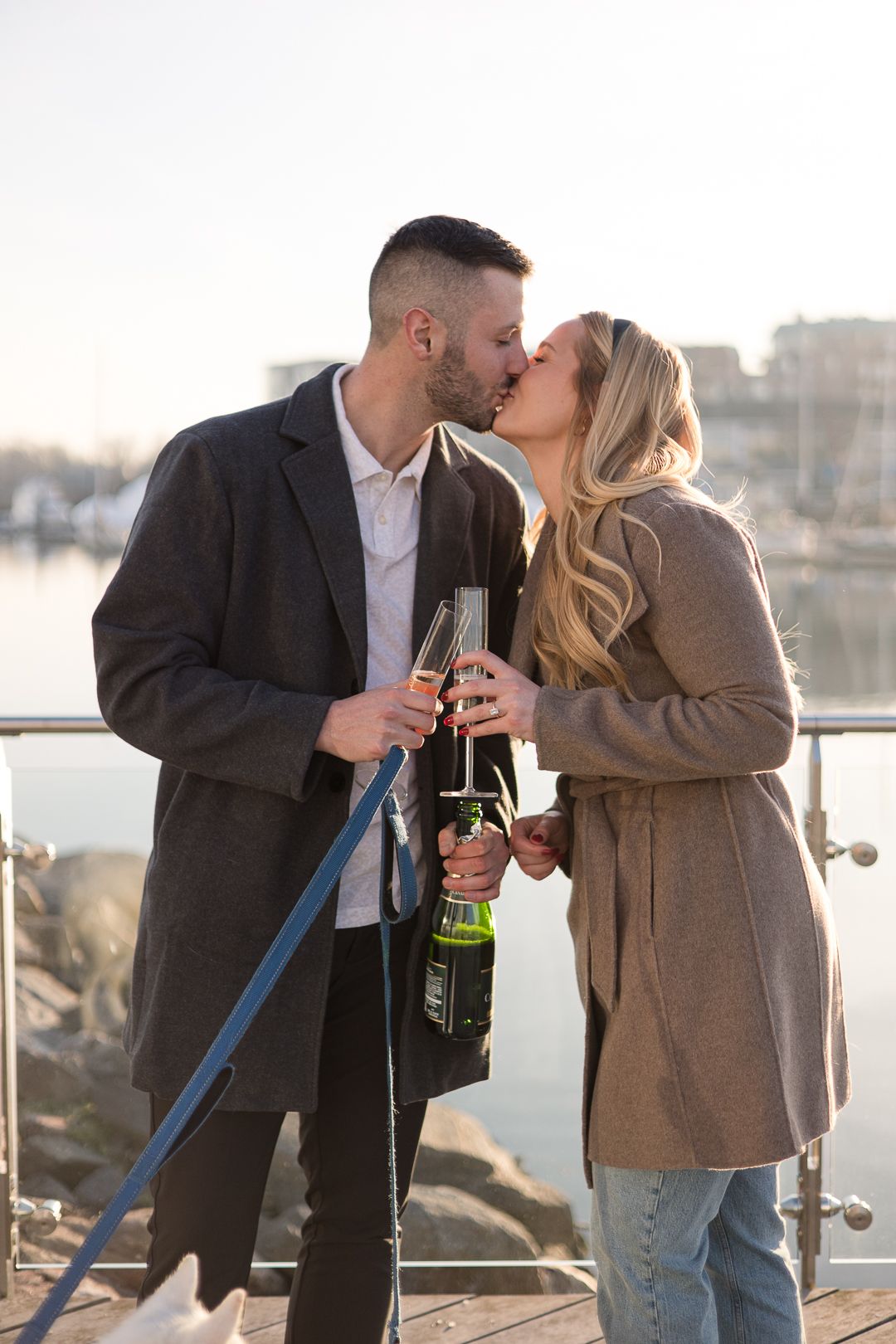 Couple toasting with champagne on marina dock during sunset celebration.