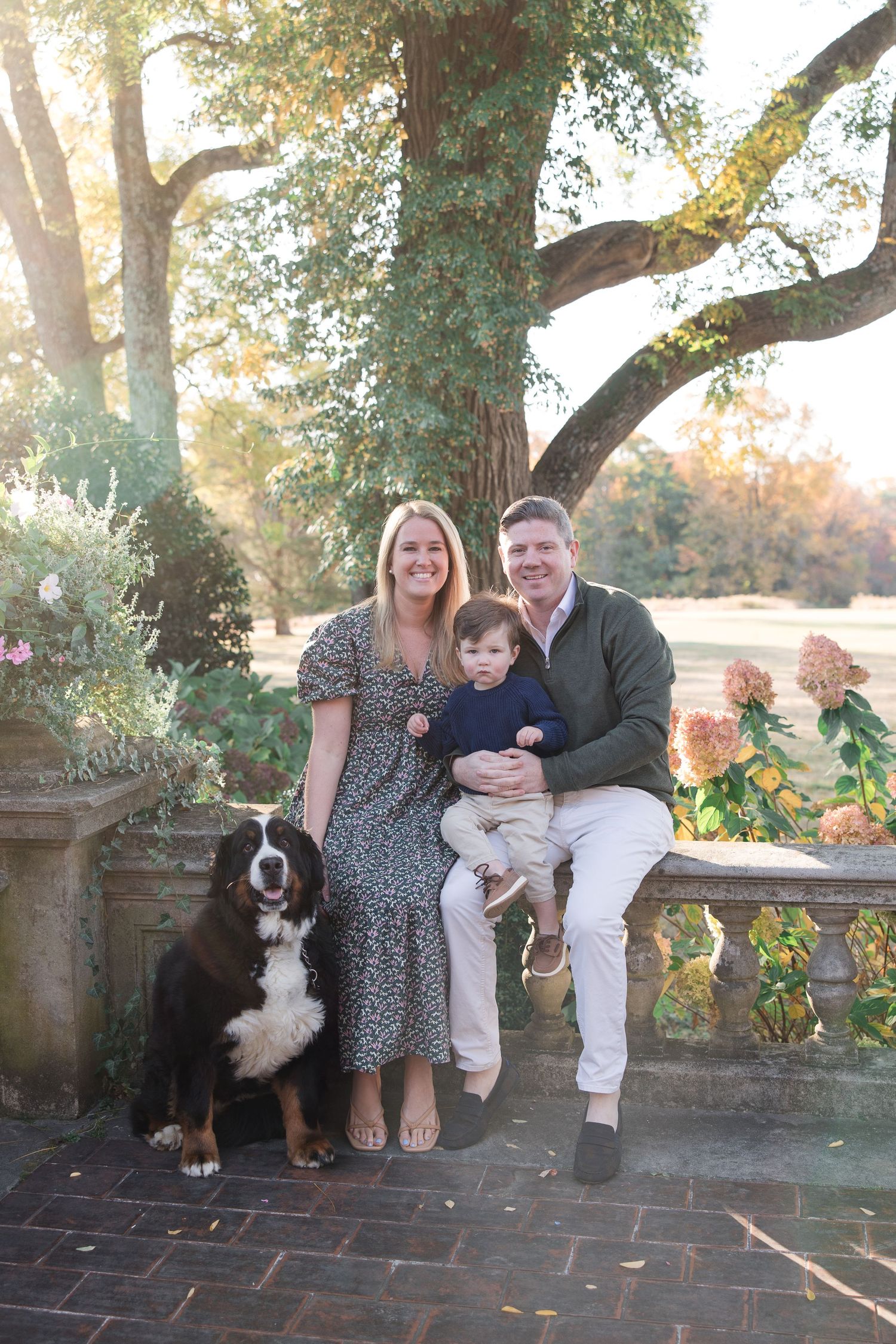 A family sits together with their Bernese Mountain Dog on stone steps surrounded by autumn foliage.