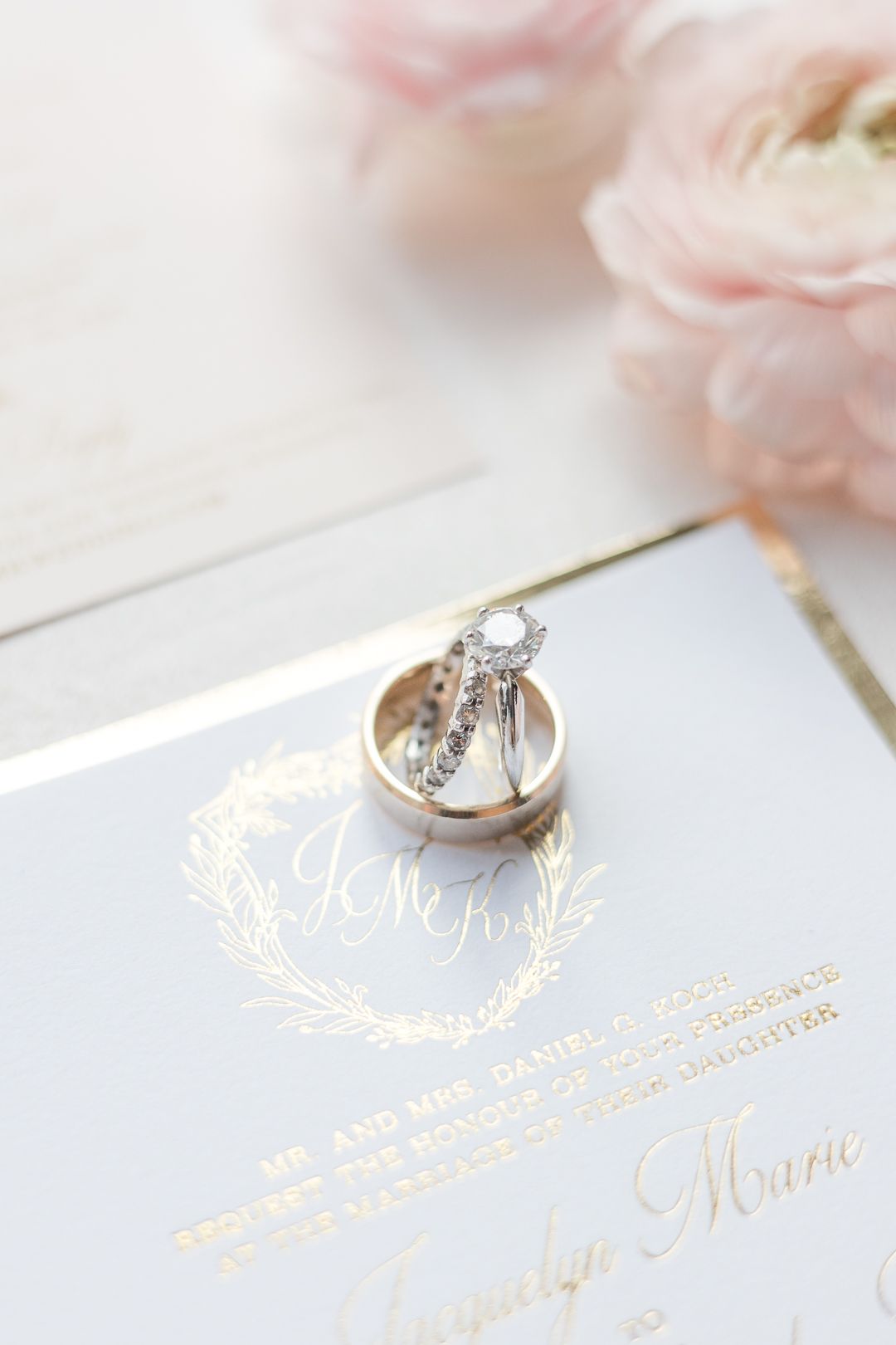 Wedding rings and invitation with gold foil lettering styled with soft pink flowers.
