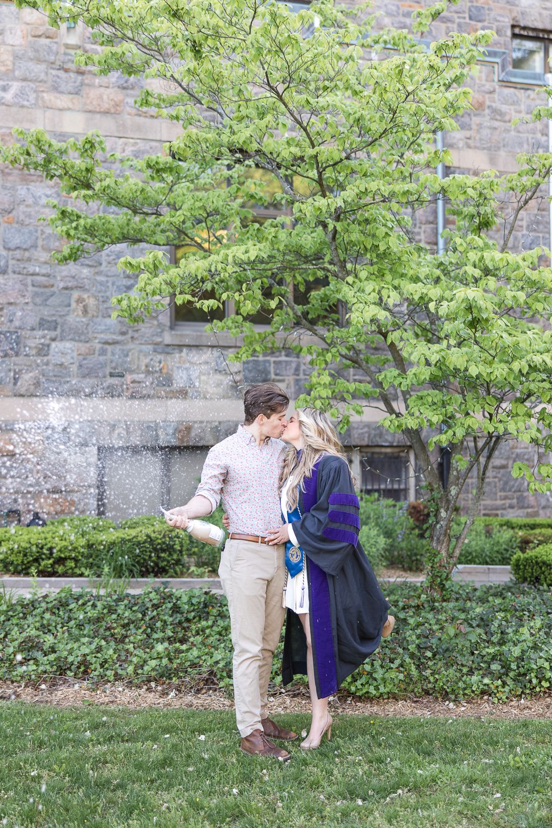 Celebratory graduation moment between two people on campus grounds near stone building.