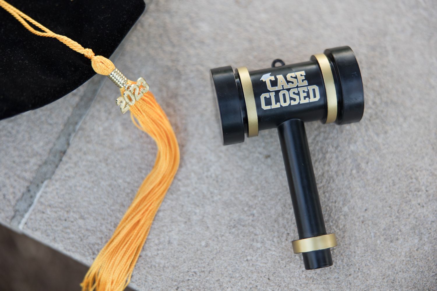 Graduation cap tassel next to decorative gavel marked 'case closed'.