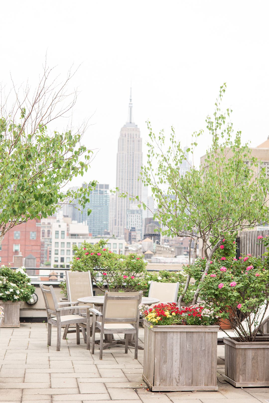 Elegant rooftop terrace with Empire State Building view featuring outdoor furniture and planted flowers.