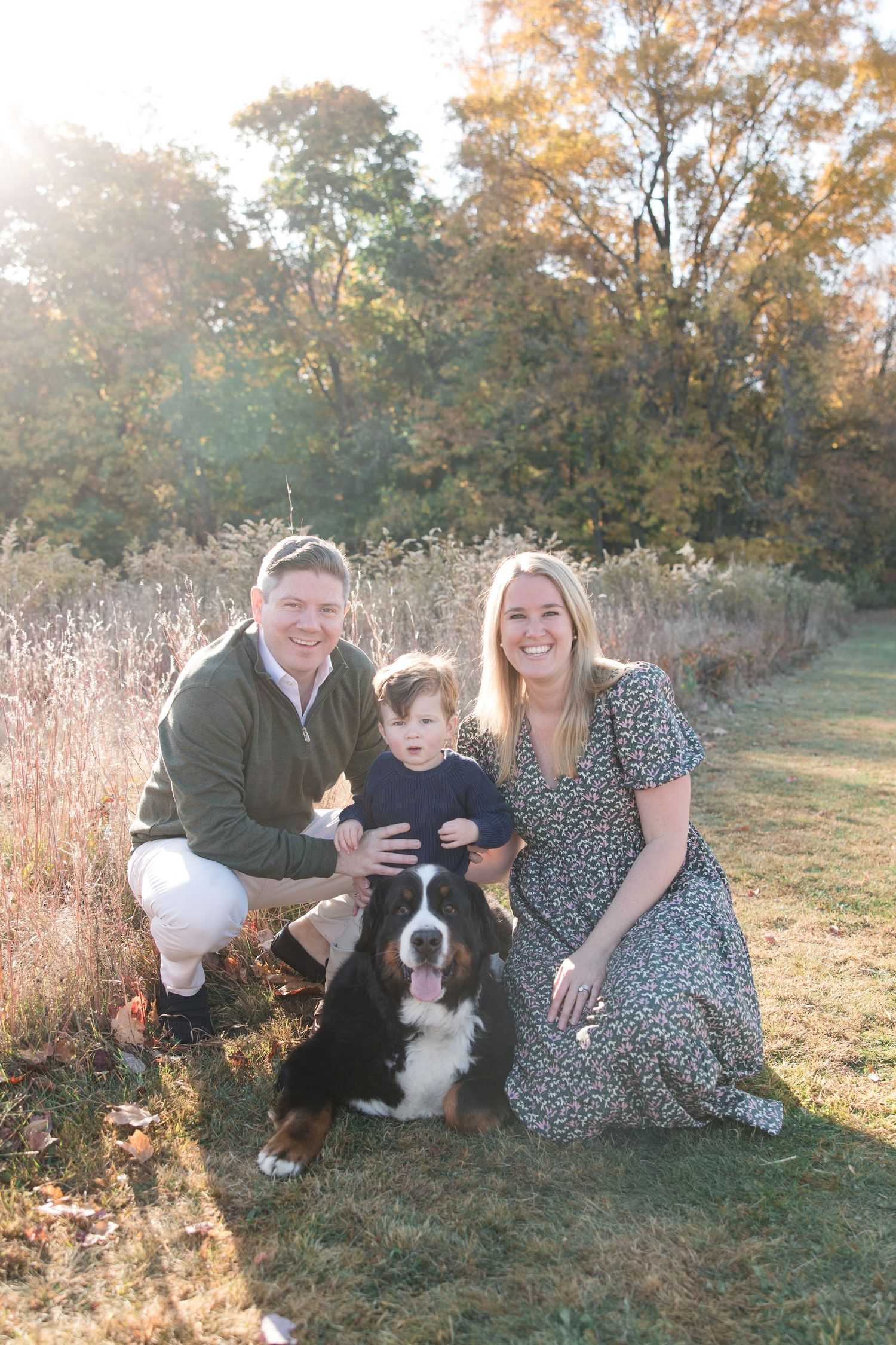 A family poses with their Bernese Mountain Dog on grass during golden hour.