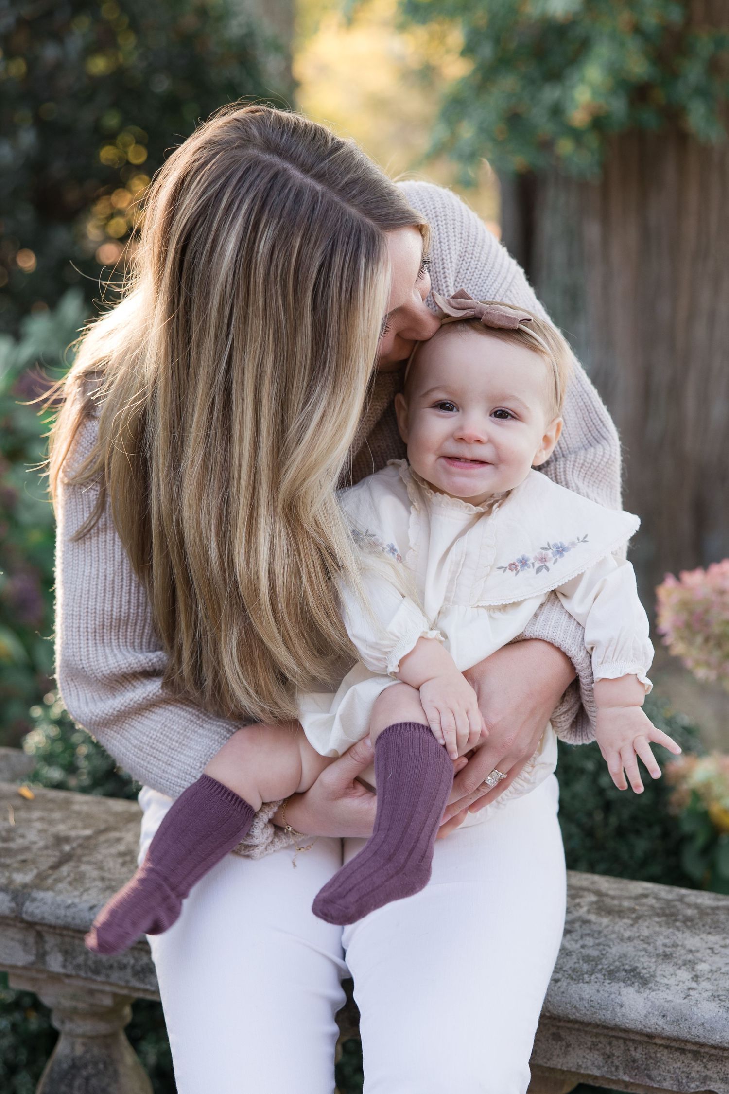 Sweet moment between parent and smiling baby in outdoor garden setting.