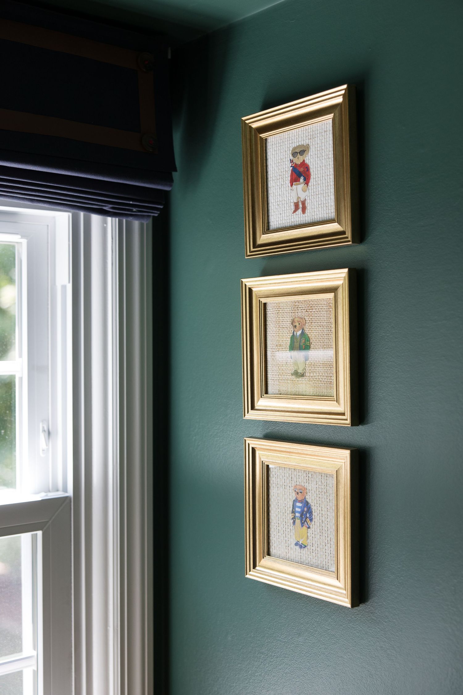 Three framed children's clothing illustrations hanging vertically on a dark green wall.