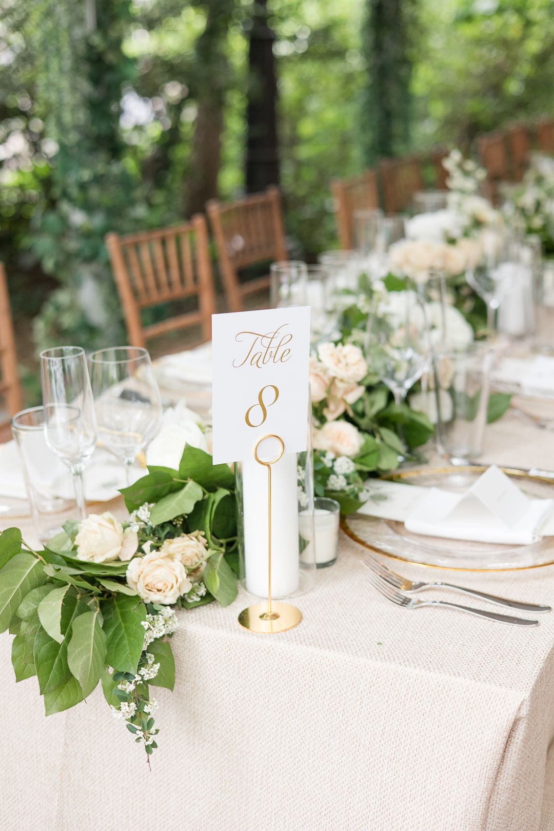 Elegant wedding table setting with gold table number and white floral centerpiece.